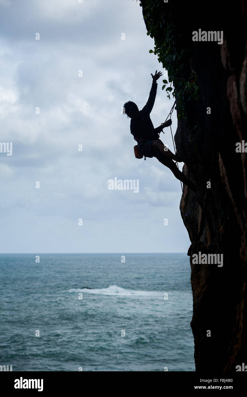 Un grimpeur est silhouetté lors d'une session d'escalade dans une zone côtière appelée Siung Beach, à Tepus, Gunungkidul, Yogyakarta, Indonésie. Banque D'Images