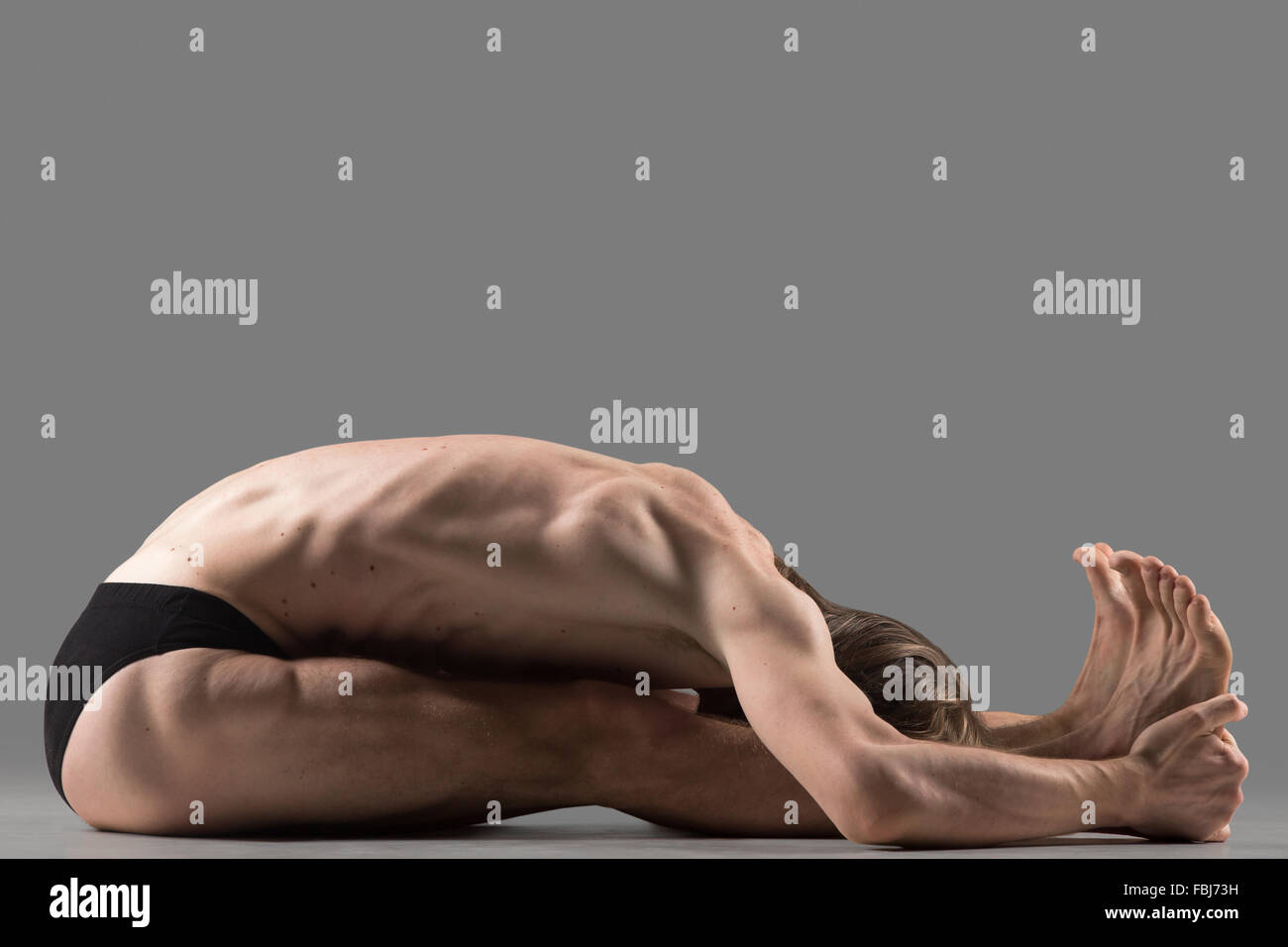 Jeune homme musclé sportif yogi assis dans paschimottanasana (Étirement dorsal intense) posent, assis vers l'avant, l'exercice de posture Banque D'Images