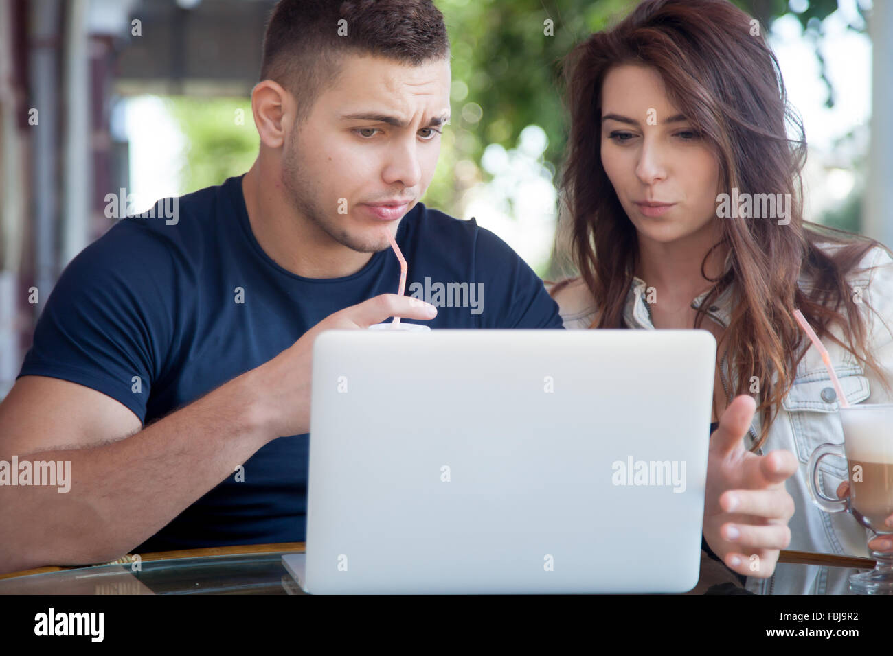 Candid portrait of young man and woman in casual clothes sitting dans street cafe, à l'aide d'un ordinateur portable, à la recherche à l'écran avec choqué ex Banque D'Images