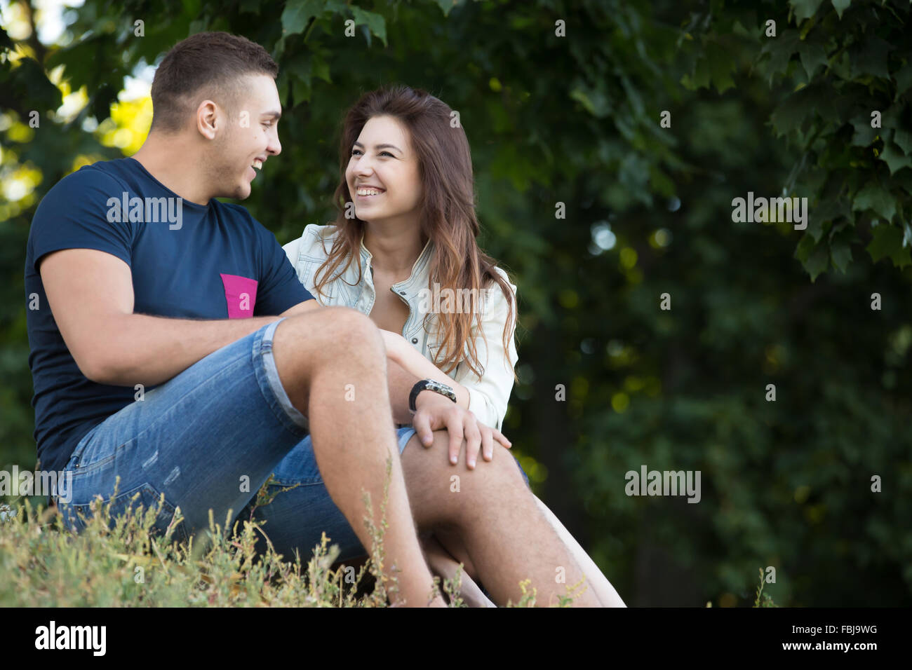 Portrait of beautiful young couple in love portant les tenues de détente dans parc, assis ensemble sur le terrain sur les s Banque D'Images