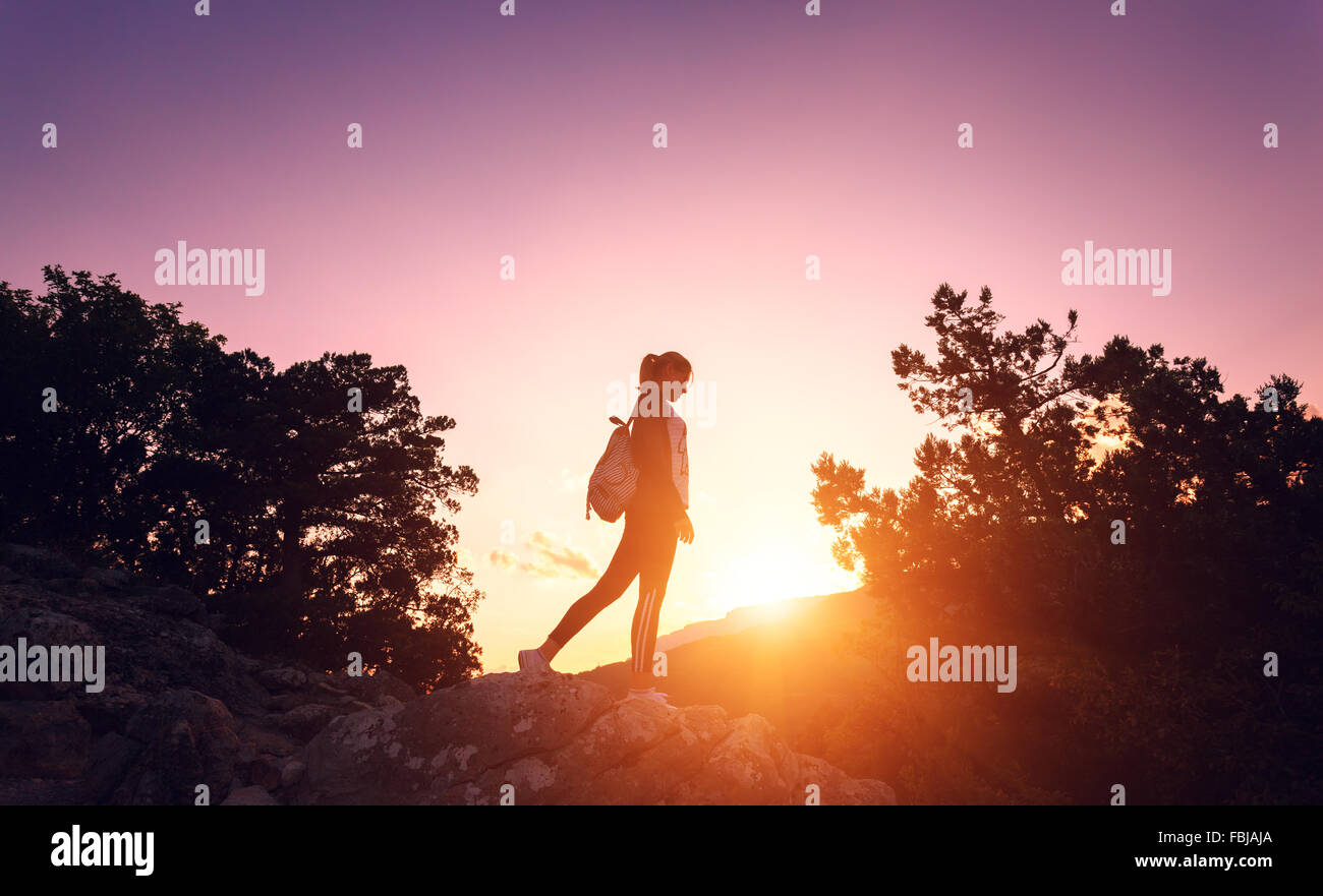 Silhouette d'une jeune femme avec sac à dos au coucher du soleil dans les montagnes en été. Nature fond Banque D'Images