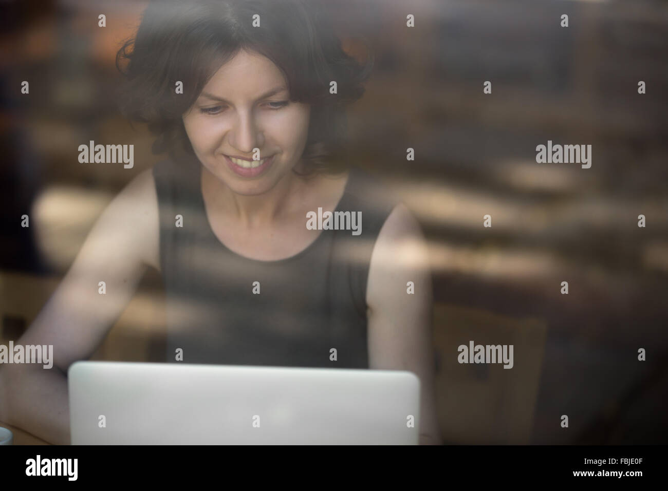 Portrait of happy smiling belle jeune femme assise en face de la fenêtre, à l'aide d'un ordinateur portable, regarder l'écran, modèle féminin Banque D'Images