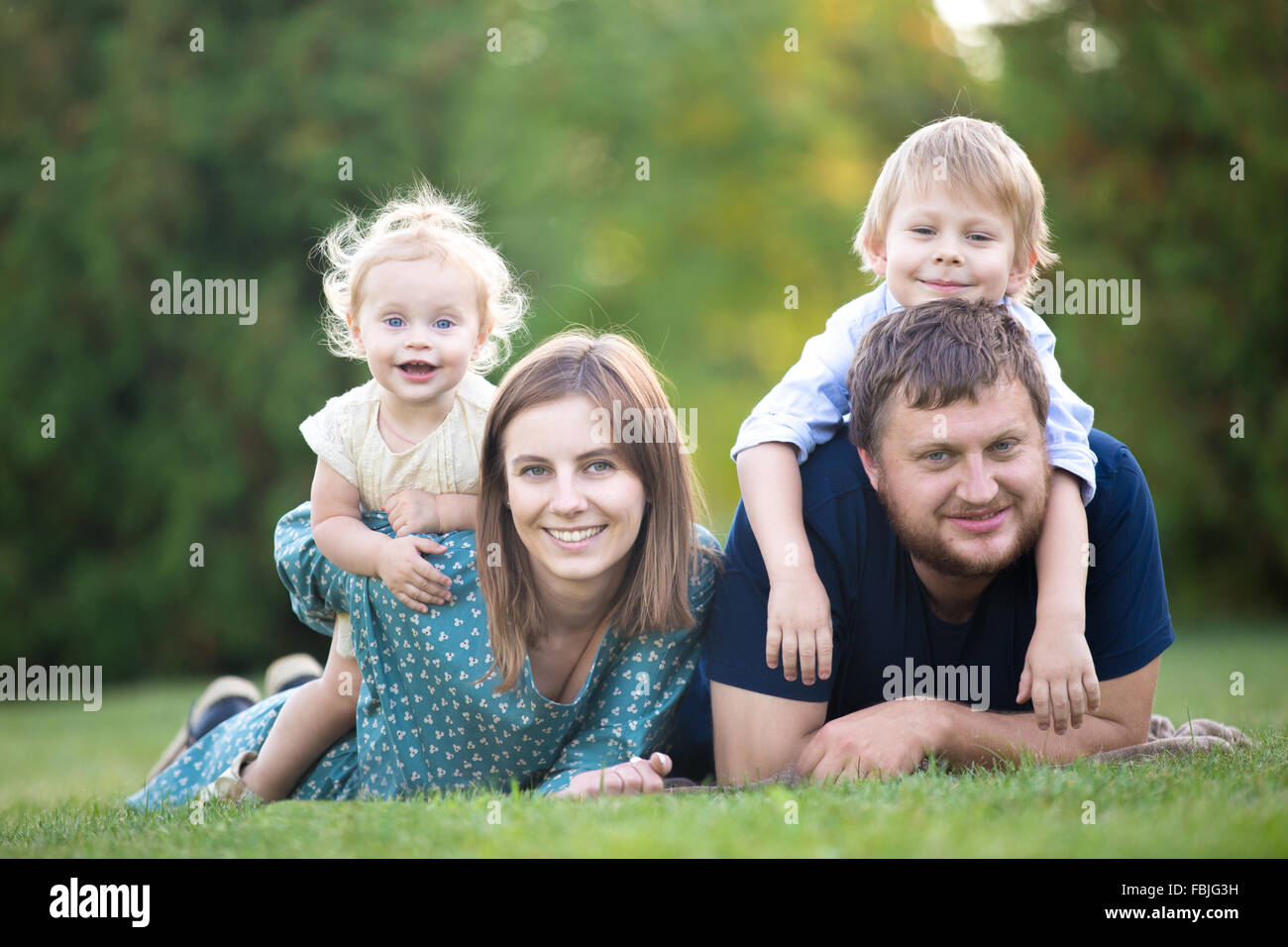 Père, mère et deux enfants lying on grass in park. Portrait of happy family of four détente sur prairie, s'amusant à Banque D'Images