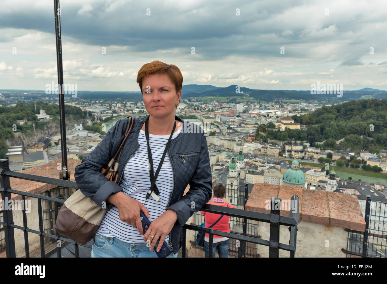 Caucasian middle aged femme bronzée avec audio guide touristique mobile électronique dans les mains se dresse contre vue aérienne sur Salzbourg Banque D'Images