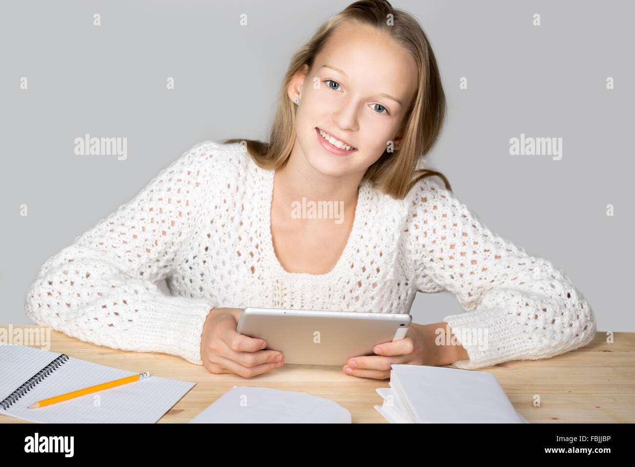 Portrait of happy casual young woman wearing white chandail tricoté, assis à table à l'aide de tablet, faire ses devoirs Banque D'Images