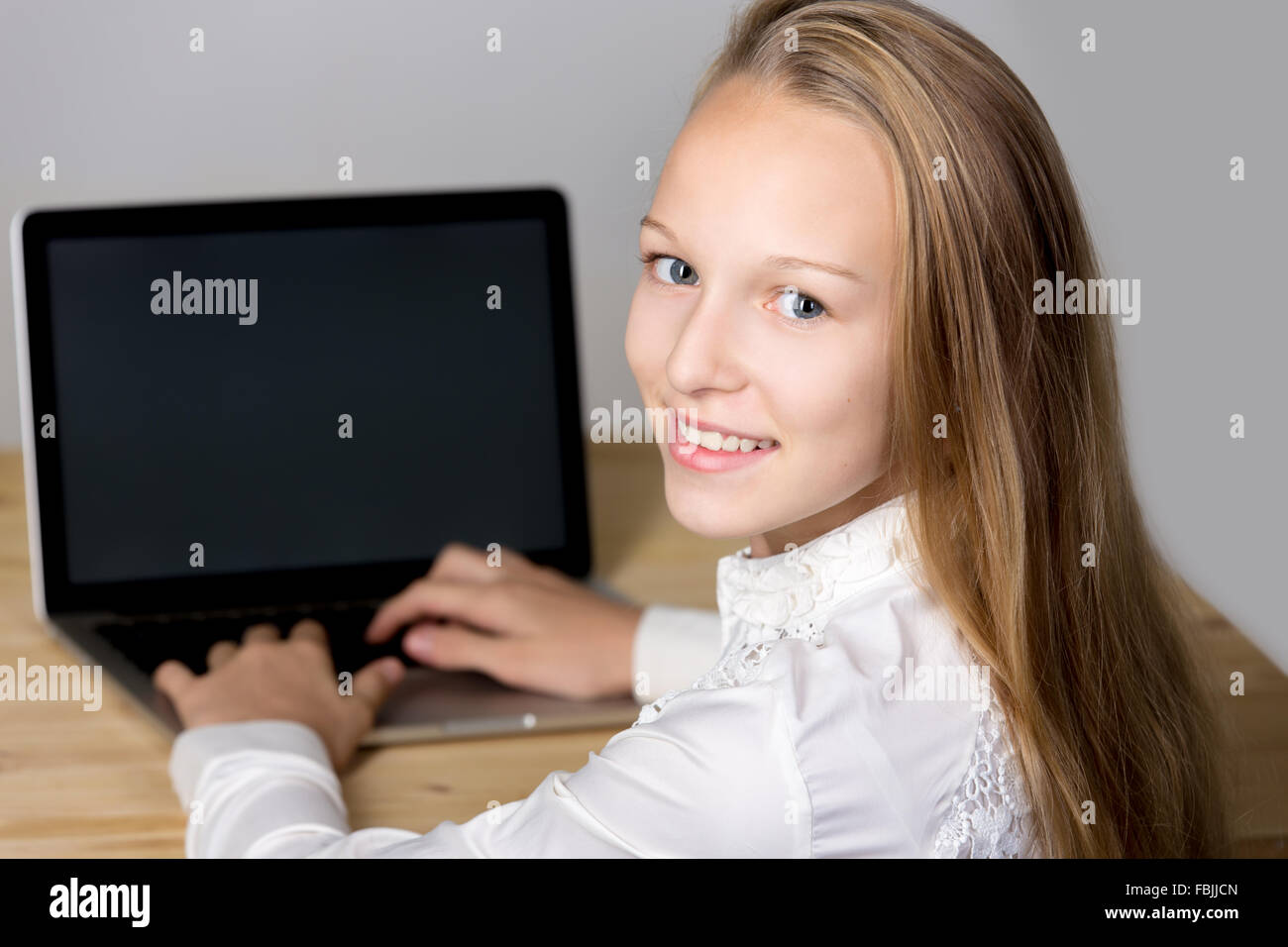 Portrait of smiling casual caucasian belle jeune femme portant uniforme blanc chemise, assis au bureau, à l'aide d'un ordinateur portable avec Banque D'Images