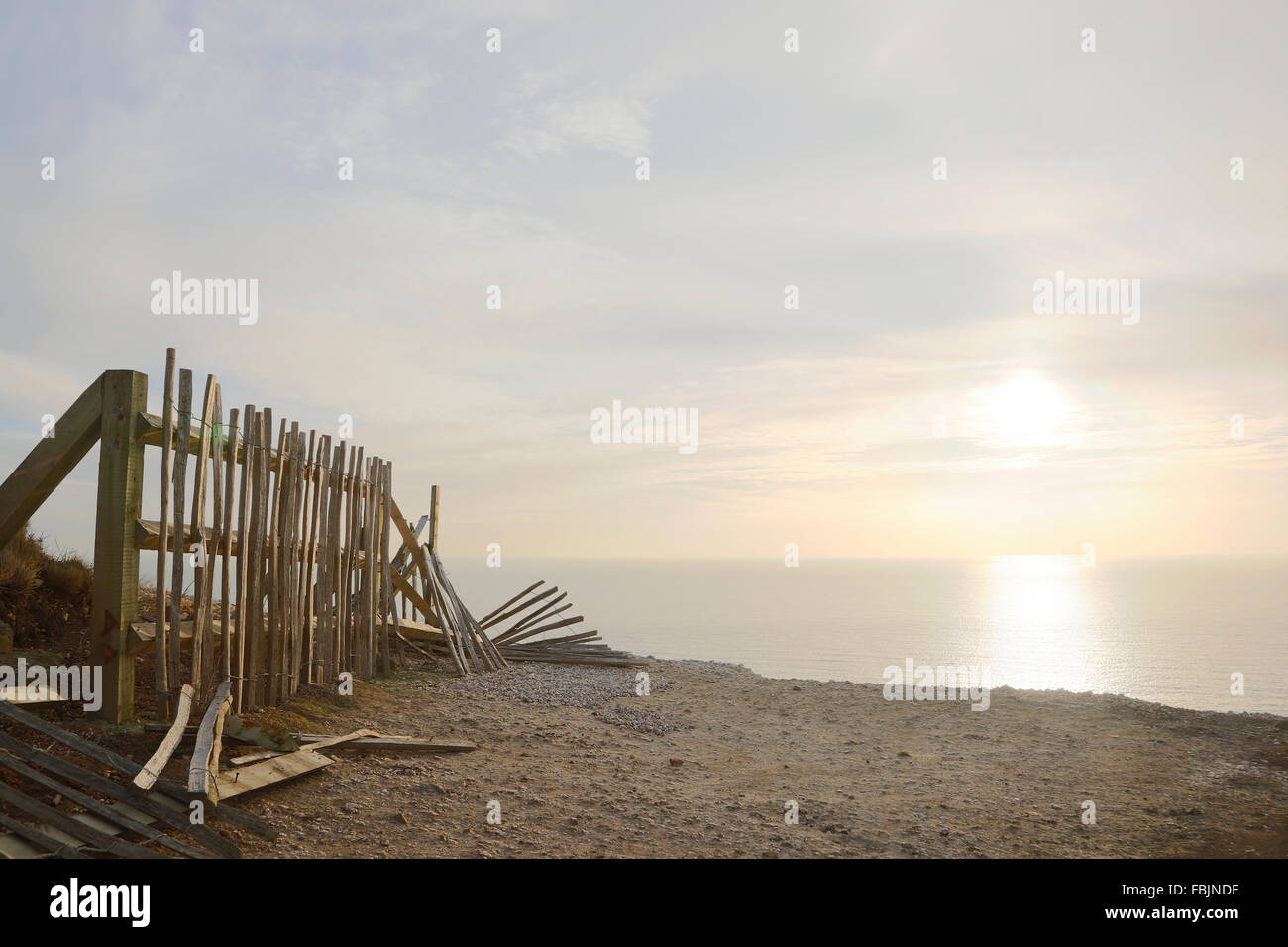 Clôture cassée tombant de la falaise de Beachy Head avec mer et soleil dans la distance. Banque D'Images