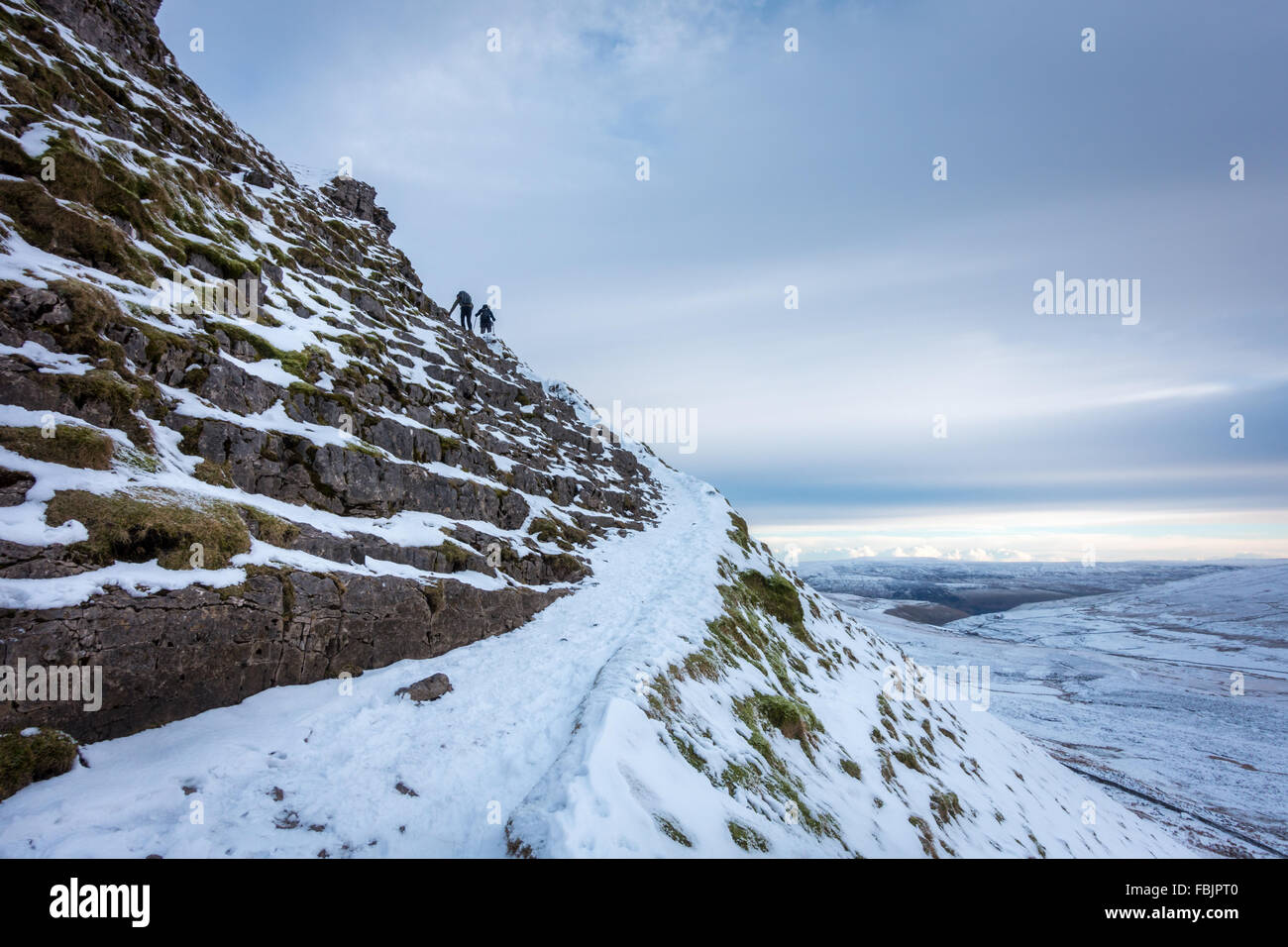 Pen-y-ghent en hiver avec deux marcheurs grimper dans la section plus raide de glace sur un jour de neige, Yorkshire Dales. Banque D'Images