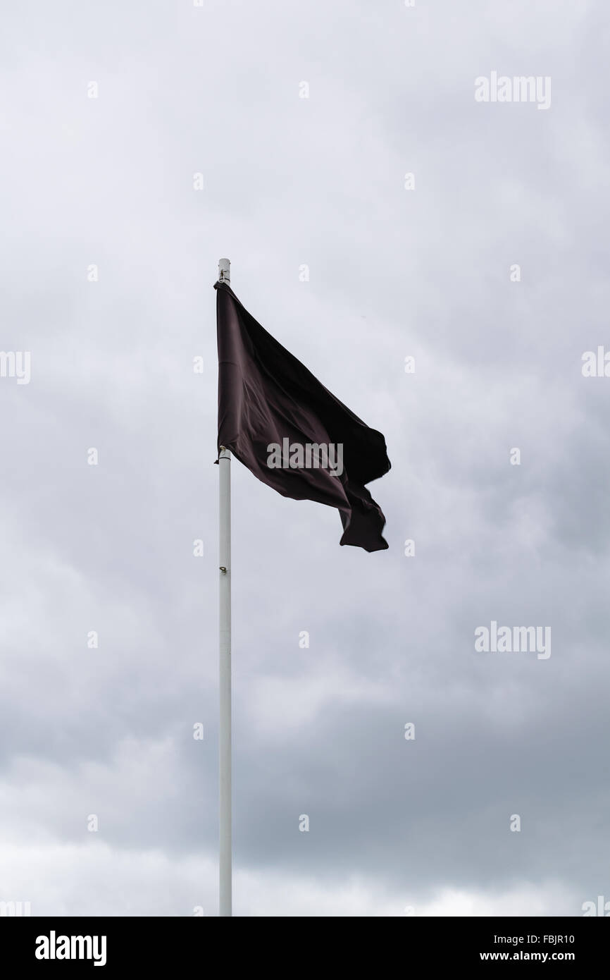 Un drapeau noir vole d'un poteau blanc. Banque D'Images