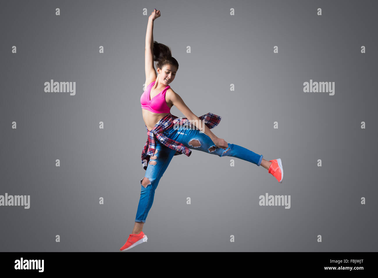 Fit belle jeune danseur hip-hop moderne woman wearing jeans déchirés, leap haut avec joie, studio, fond gris Banque D'Images