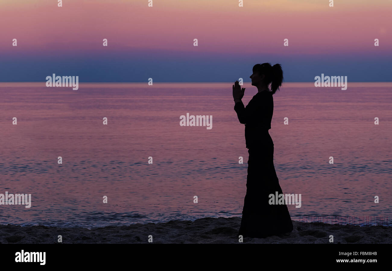 Silhouette of a woman standing on beach with hands in position de prière Banque D'Images