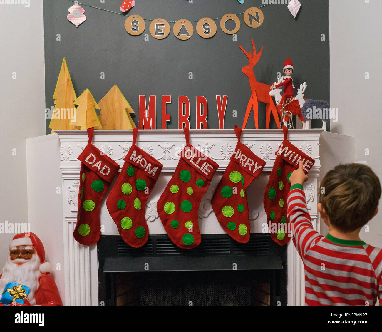 Garçon debout devant le foyer en montrant des bas de Noël et décorations Banque D'Images