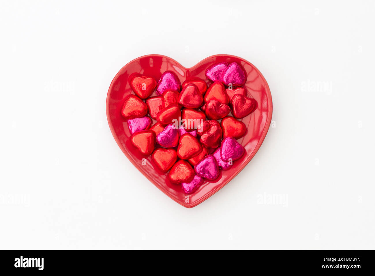 Un rouge, en forme d'coeur saint-valentin assiette pleine de chocolats sur un fond blanc. Banque D'Images