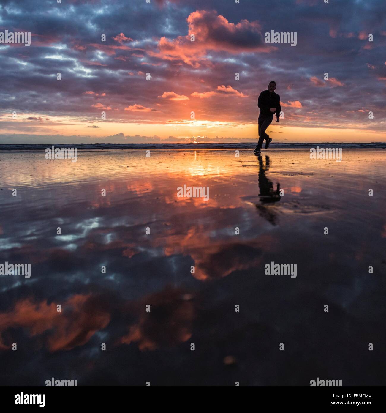 Silhouette d'un homme qui court le long de plage au coucher du soleil Banque D'Images