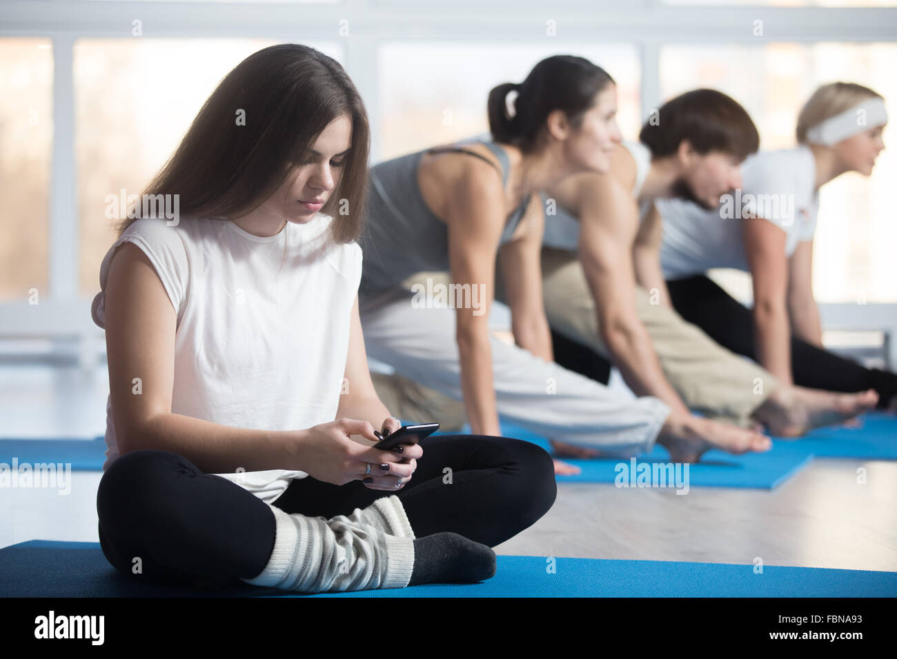 Fatigué ou paresseux, femme assise en tailleur, le repos au cours de la pratique de sports club, utilisation du téléphone, la lecture, l'envoi ou la saisie Banque D'Images