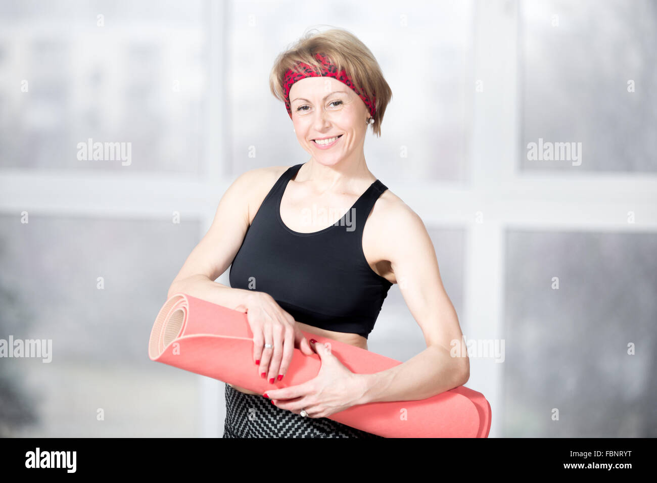 Portrait intérieur de cheerful attractive monter senior woman posing holding fitness rouge mat, travaillant à l'sports club class, heureux Banque D'Images