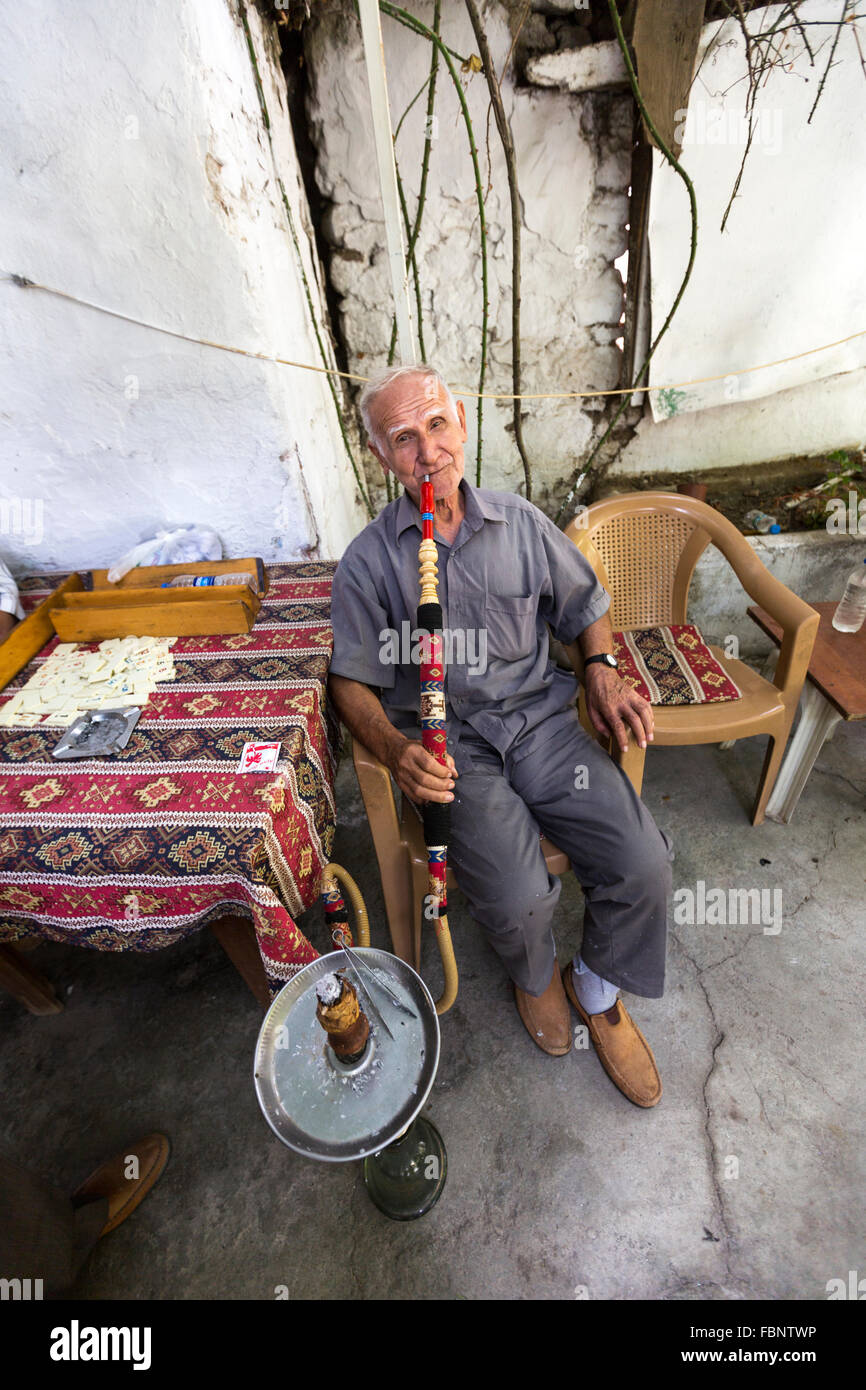 Vieil homme assis à l'extérieur d'un café fumant un narguilé de la Turquie de l'eau tuyau de fumée dans le vieux bazar, Pergame Bergama. Banque D'Images