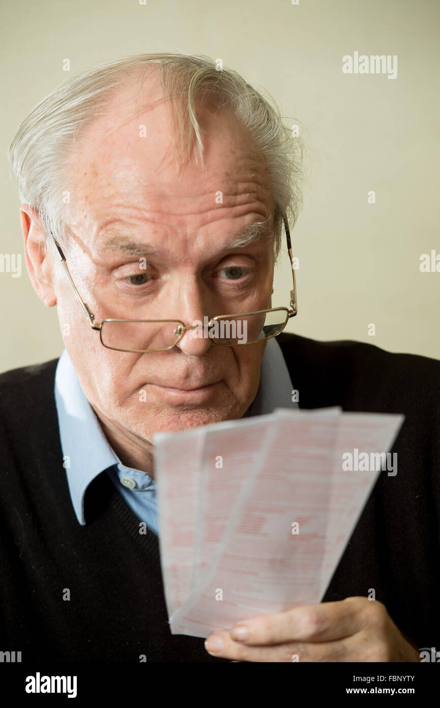 Un homme âgé regarde par-dessus ses lunettes dans un confusément à des billets de loterie Banque D'Images