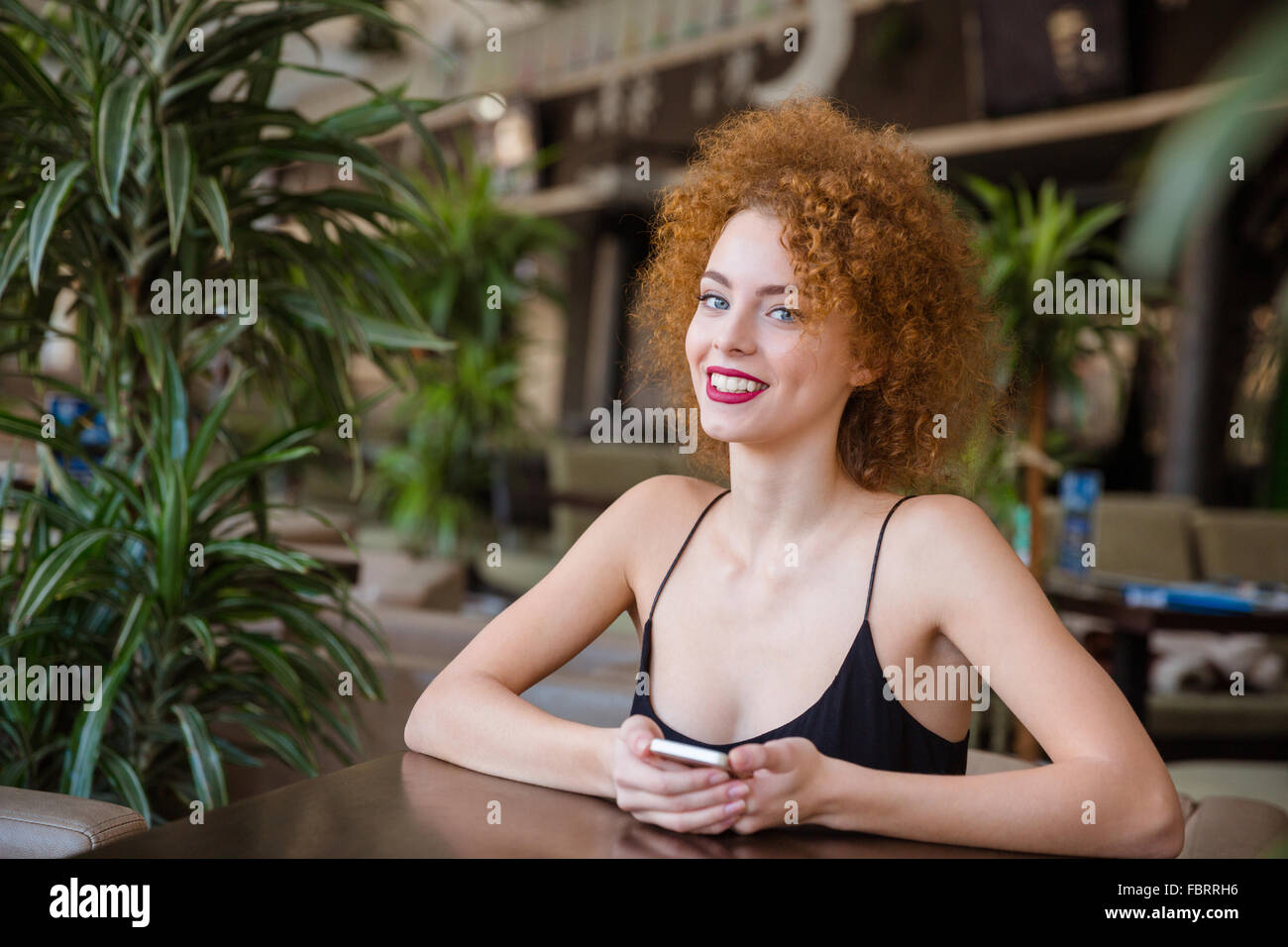 Portrait of a smiling redhead femme avec les cheveux bouclés à la table dans un restaurant et looking at camera Banque D'Images