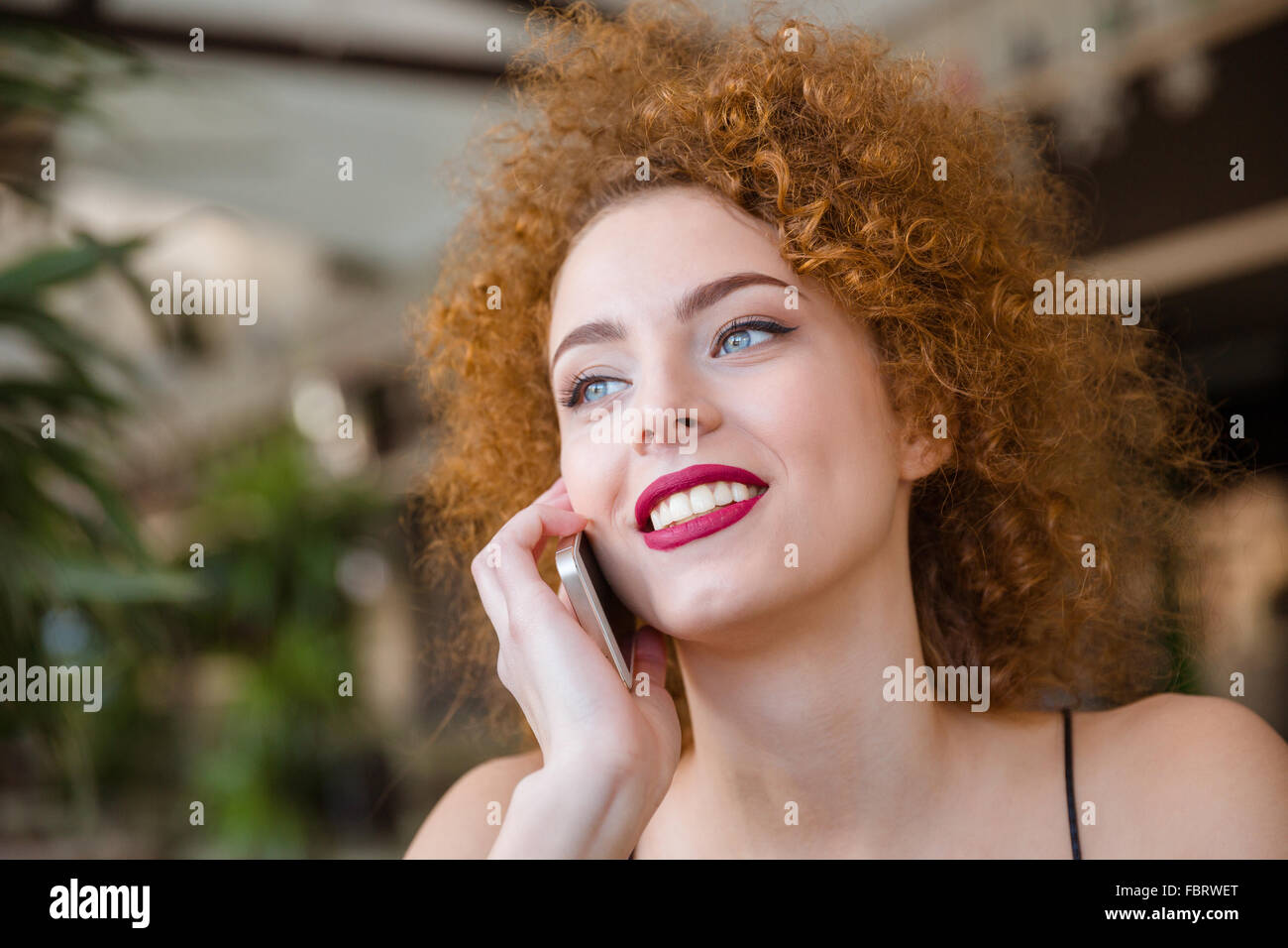 Smiling redhead femme avec les cheveux bouclés à parler au téléphone et à l'écart Banque D'Images