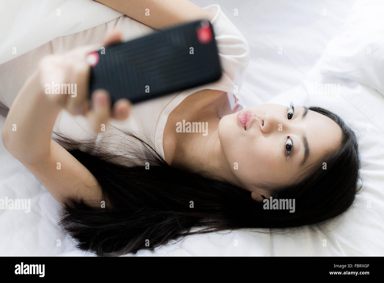 Femme au lit, l'utilisation de smartphone pour prendre un selfies Banque D'Images