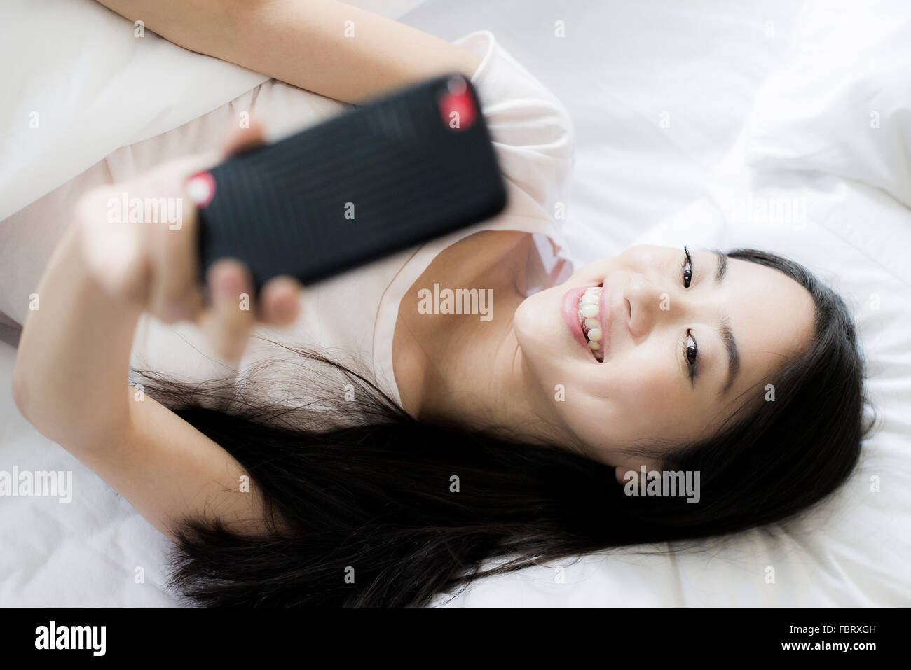 Femme au lit, l'utilisation de smartphone pour prendre un selfies Banque D'Images