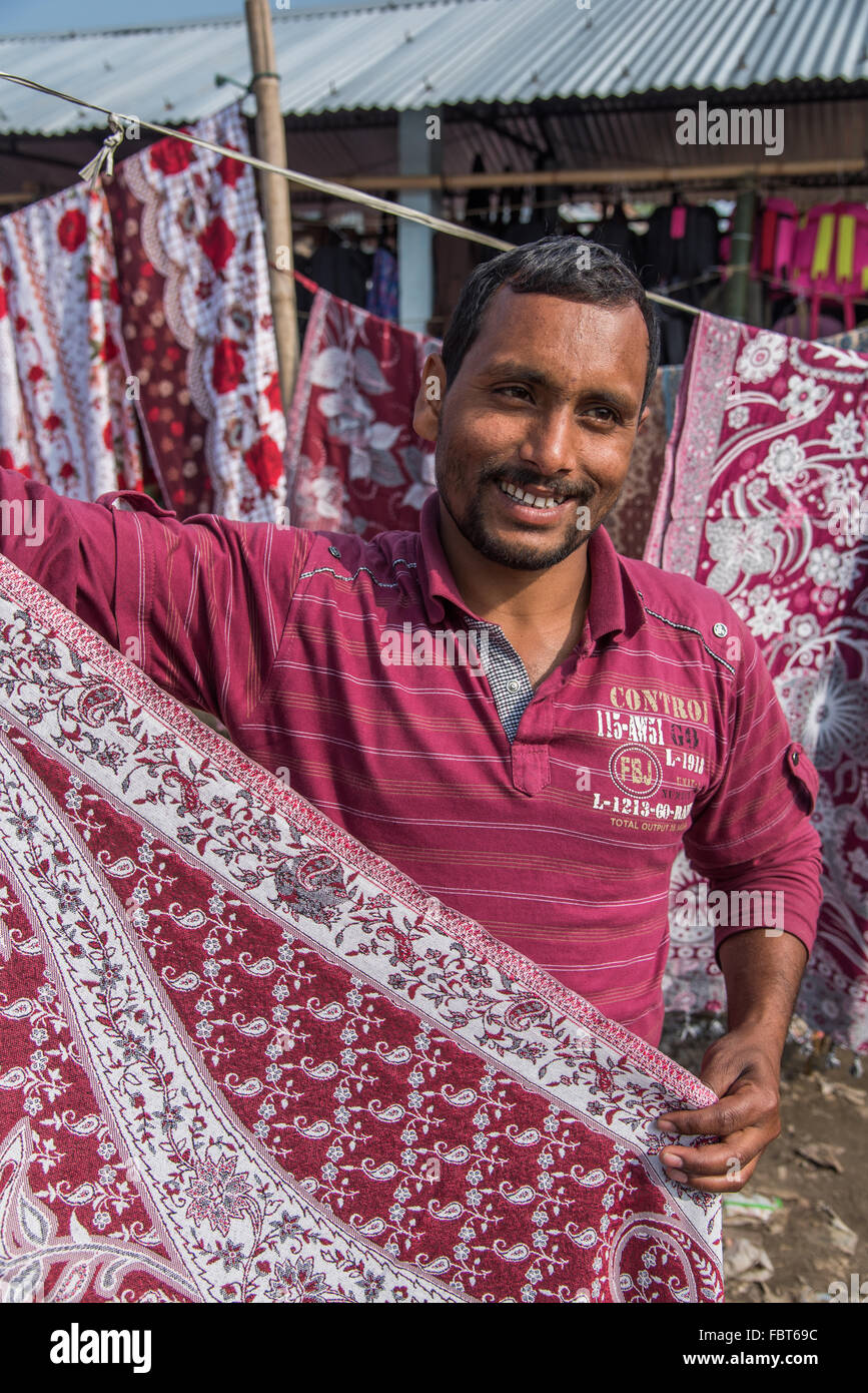 Marché indien. Un marchand de marché masculin détient un sari à vendre au marché du samedi Balipara, près de Tezpur, Assam, INDE. Banque D'Images