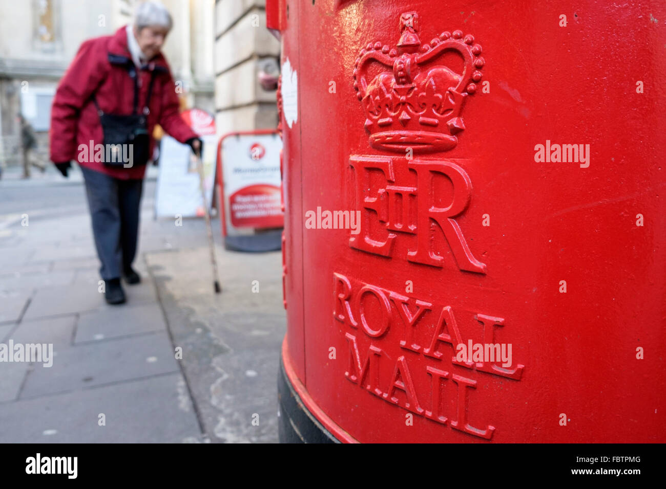 Une vieille dame passe devant une boîte rouge dans la région de Bath, Royaume-Uni. Banque D'Images