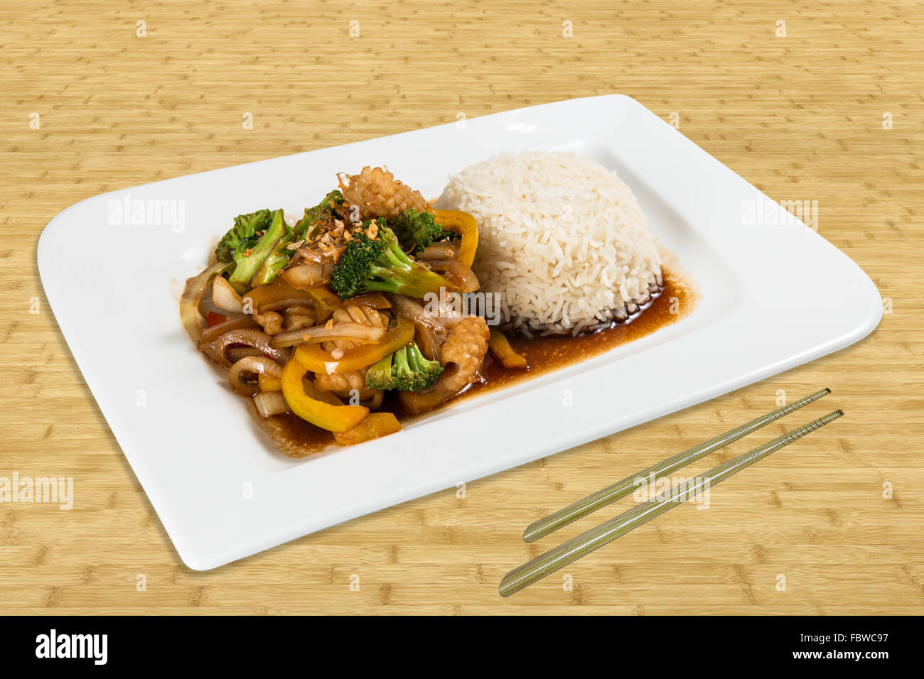 Cuisine chinoise classique sur une plaque debout sur une table avec légumes et riz sauce brune. Baguettes, l'arrière-plan avec le bois. Banque D'Images