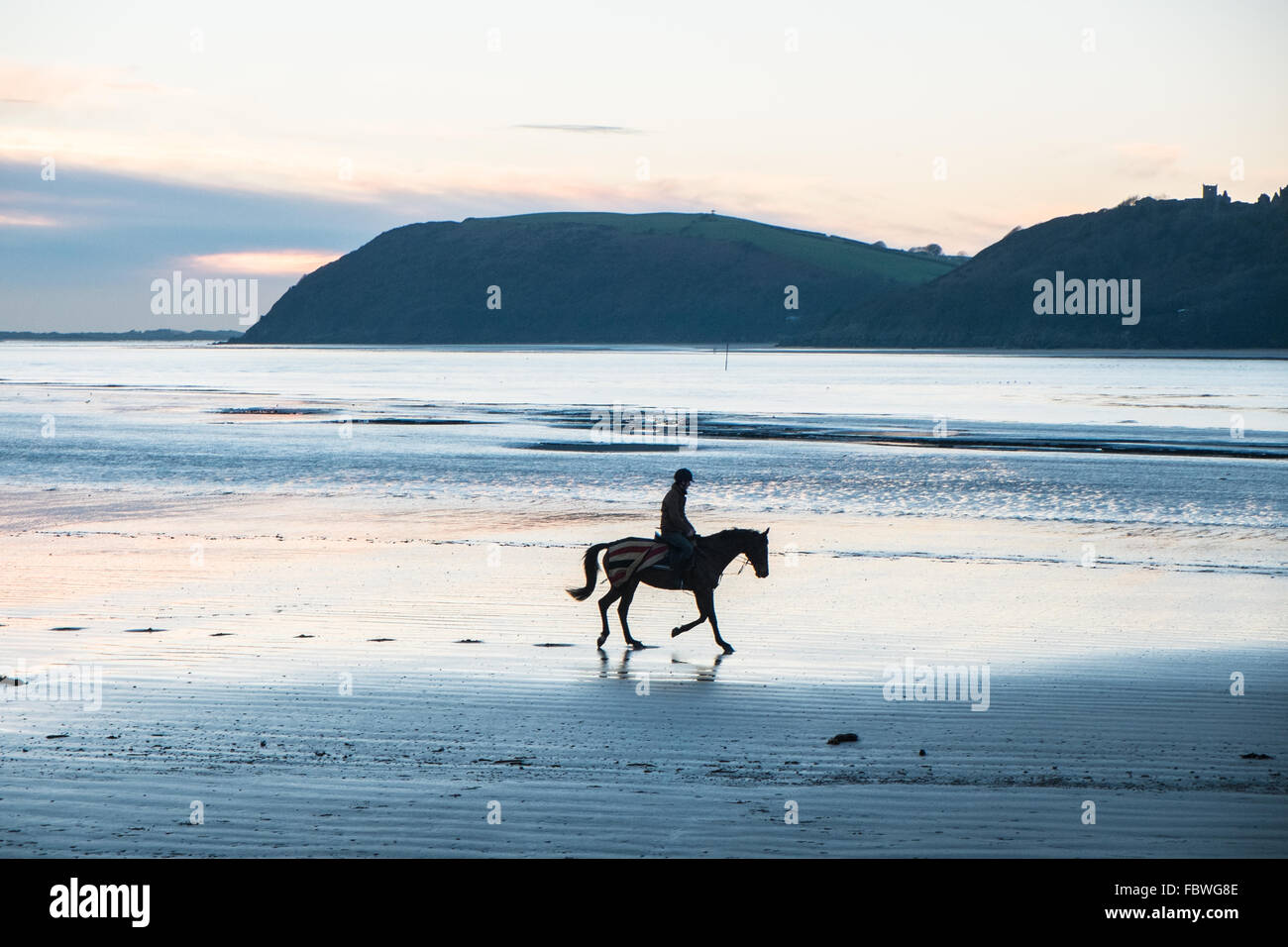 Ferryside, Carmarthenshire, Pays de Galles, Royaume-Uni. 19 janvier, 2016. Après des jours de pluie sur une journée ensoleillée au coucher du soleil/coucher du soleil.Si amèrement froid un jockey son cheval galope sur la plage vide à Ferryside, Carmarthenshire, Pays de Galles, U.K.Llanstephan Castle en arrière-plan. Crédit : Paul Quayle/Alamy Live News Banque D'Images