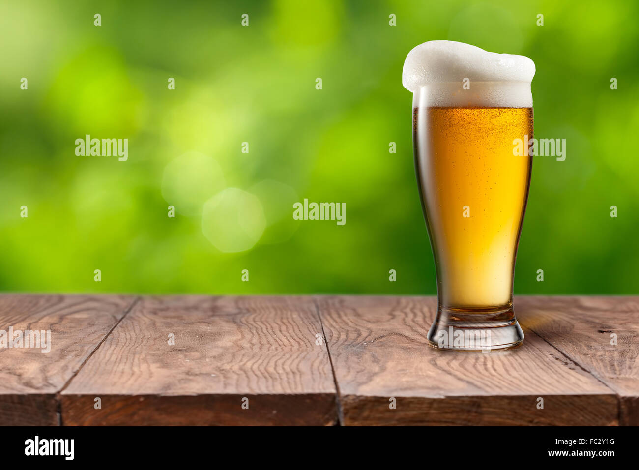 La bière dans le verre sur la table en bois contre green Banque D'Images