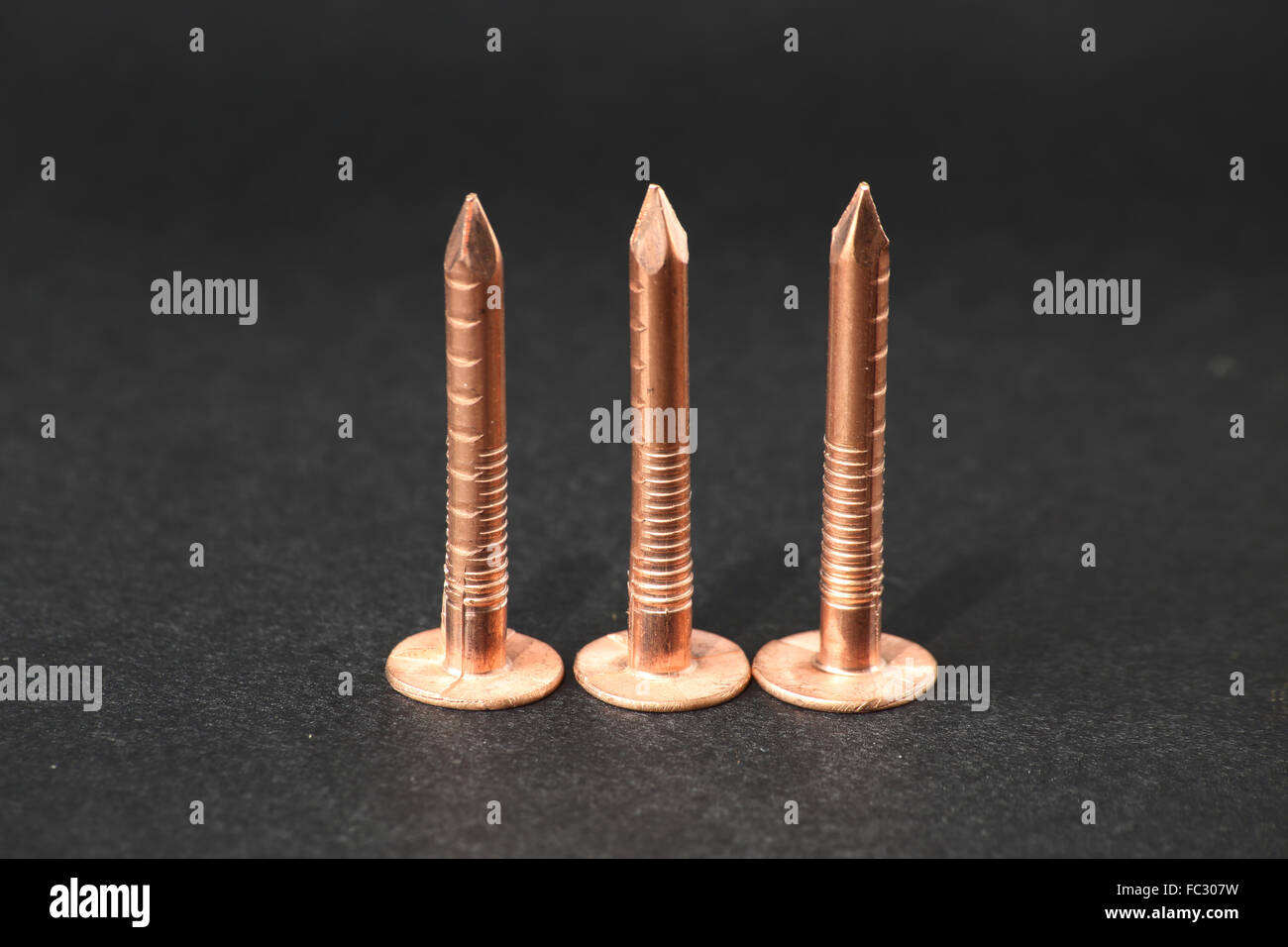 Studio close-up shot de trois clous à toiture de cuivre sur un fond noir Banque D'Images
