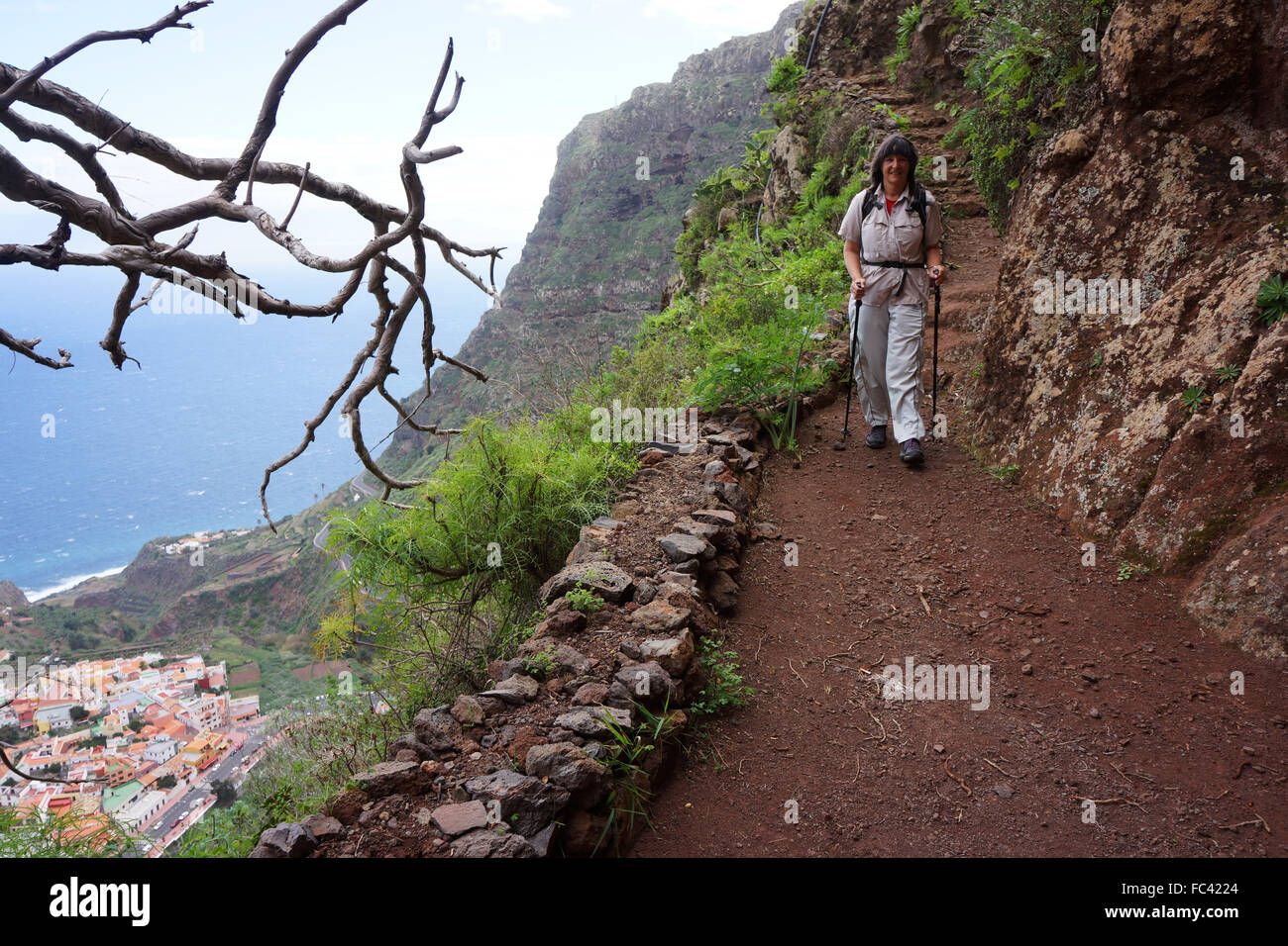 Randonneur sur sentier à travers le mur rouge au-dessus de l'île de La Gomera, Agulo, Canaries, Espagne Banque D'Images