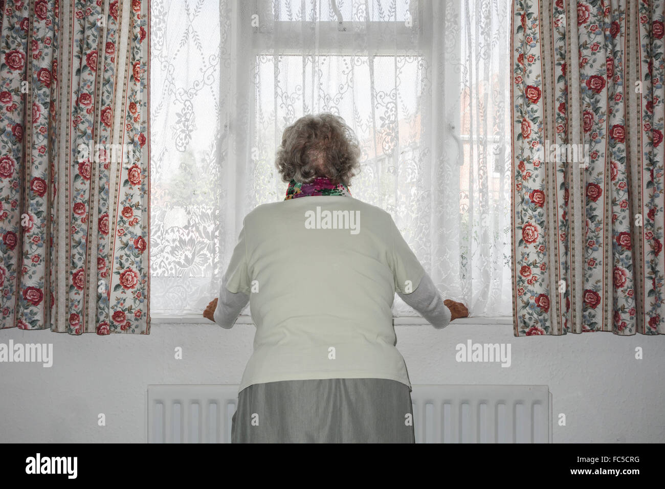 Femme de quatre-vingt-dix ans avec radiateur à la main regardant hors de la fenêtre. ROYAUME-UNI. Coronavirus, auto-isolement, distanciation sociale, quarantaine... concept Banque D'Images