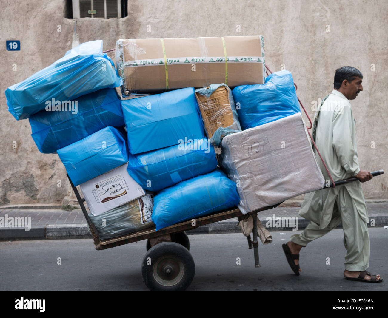 Souk de Dubaï : homme tirant une charrette pour le transport de marchandises. Banque D'Images