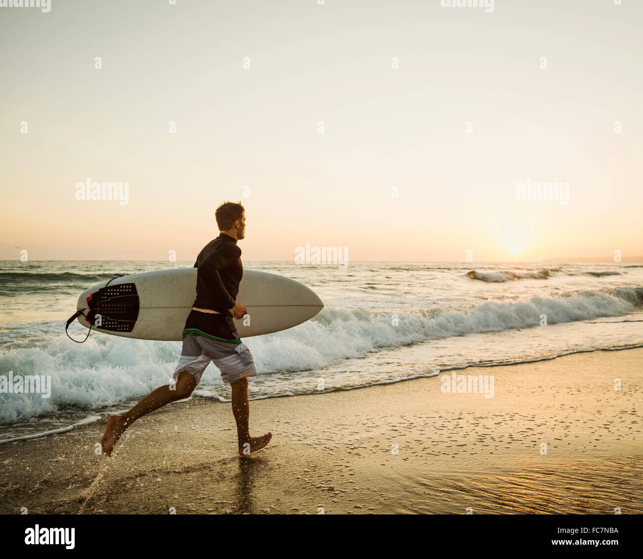 Caucasian man carrying surfboard on beach Banque D'Images