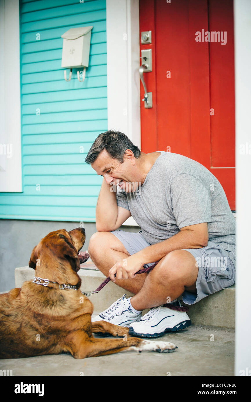 Caucasian man petting dog in front stoop Banque D'Images