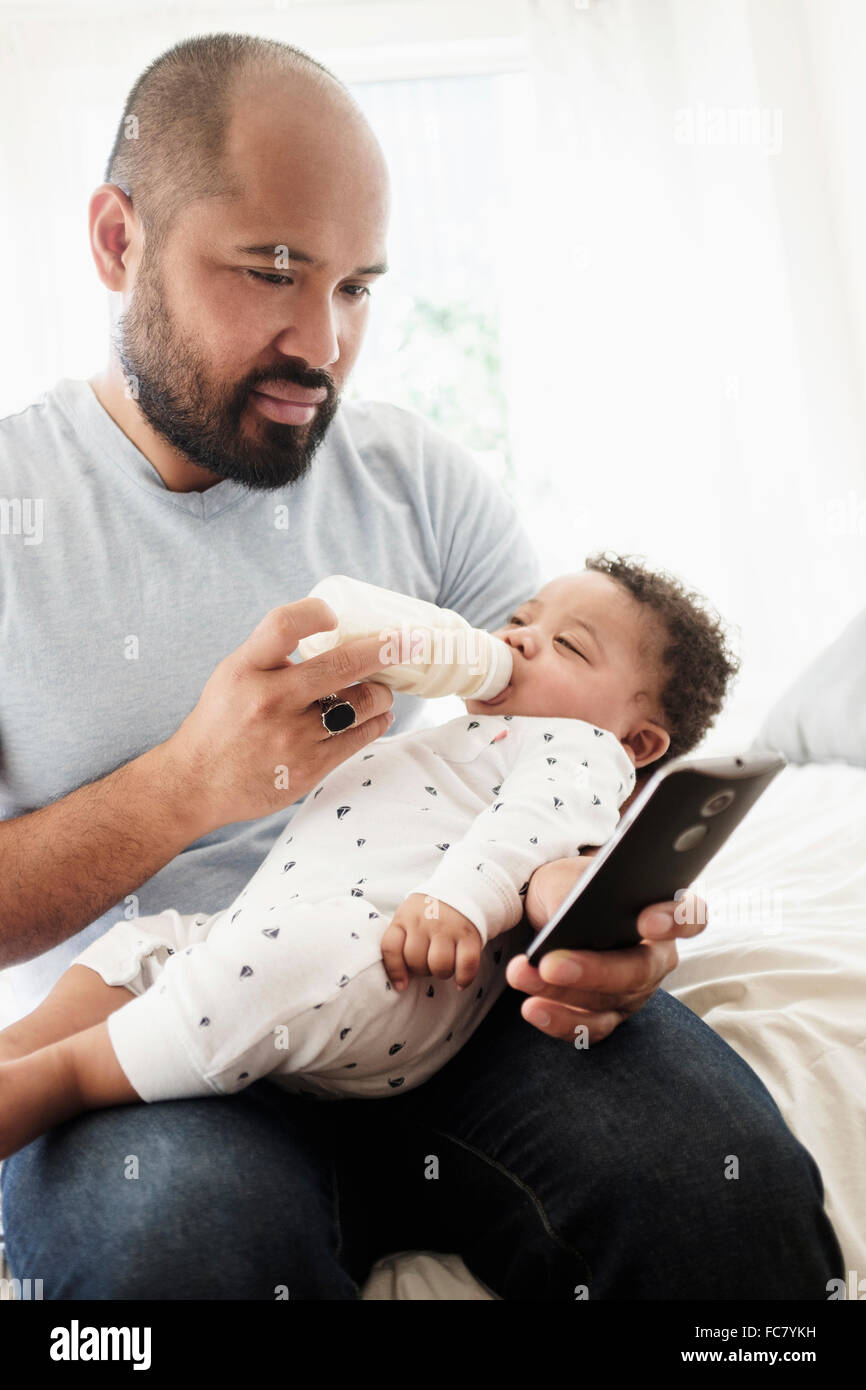 Père et fils bébé biberon using cell phone Banque D'Images