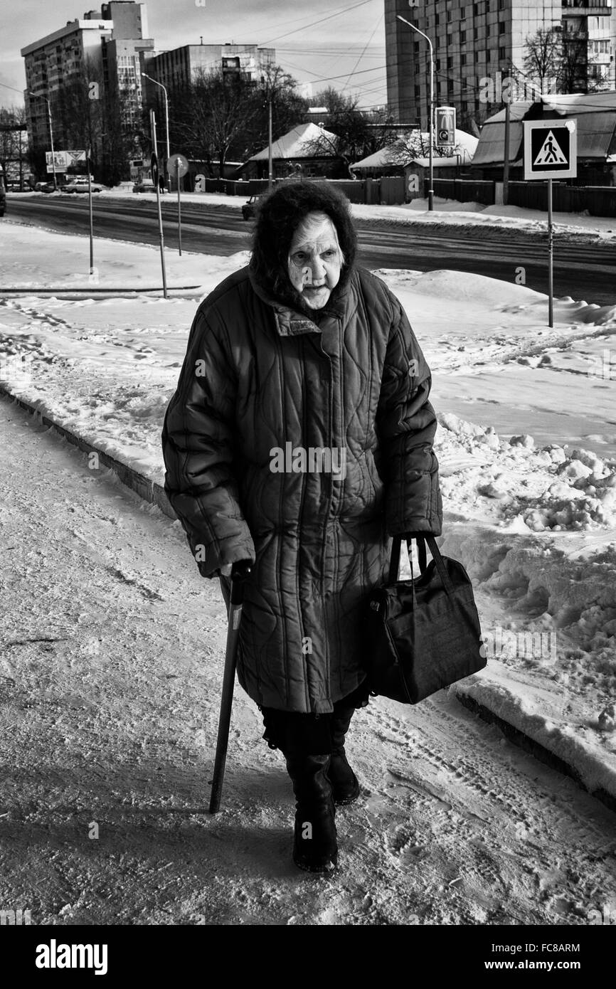 Seule vieille femme promenades le long d'un chemin avec l'aide de son bâton de marche. L'hiver la neige et la glace Banque D'Images