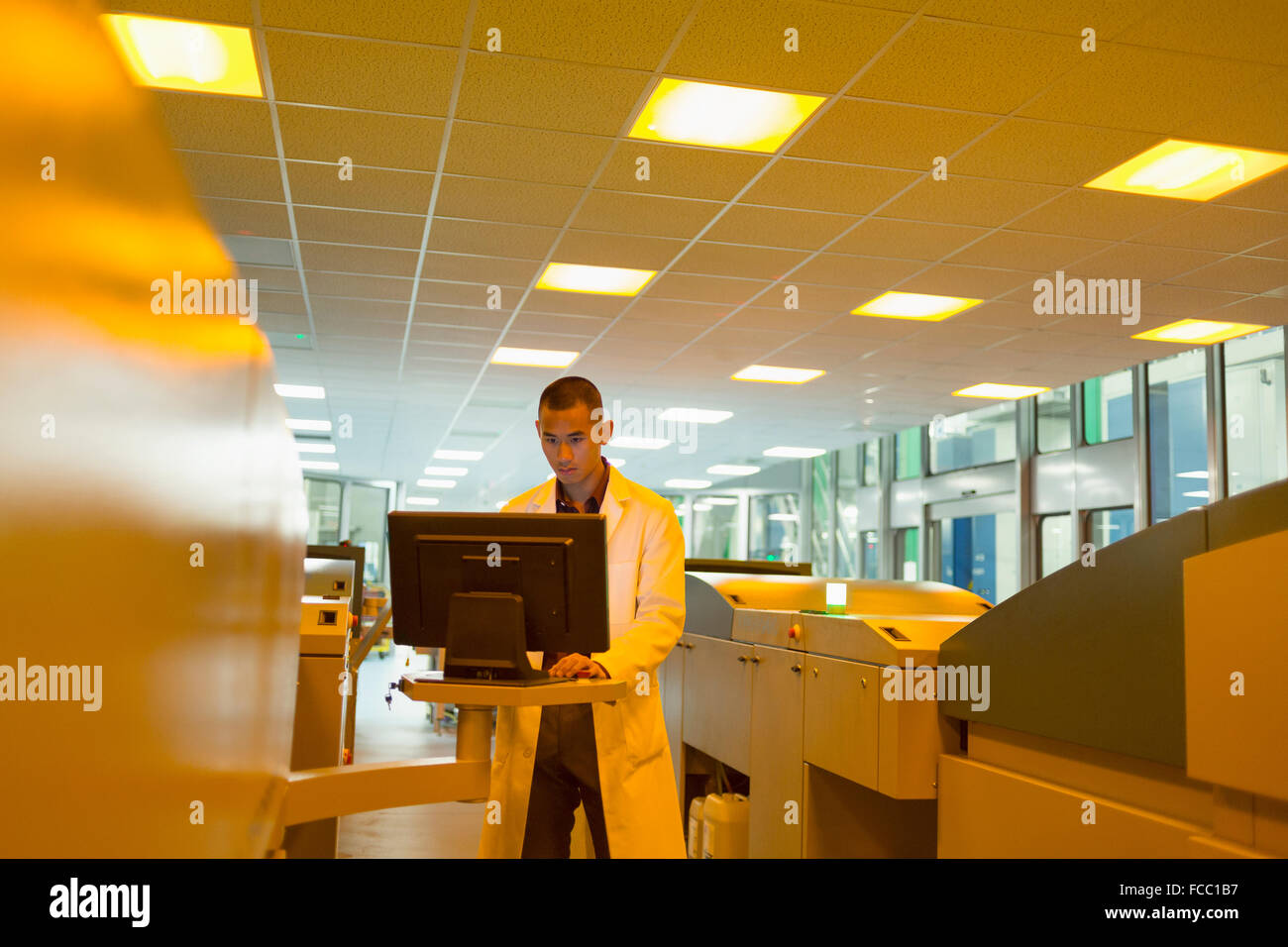 Travailleur en manteau de laboratoire à l'ordinateur entre les imprimantes dans une imprimerie Banque D'Images