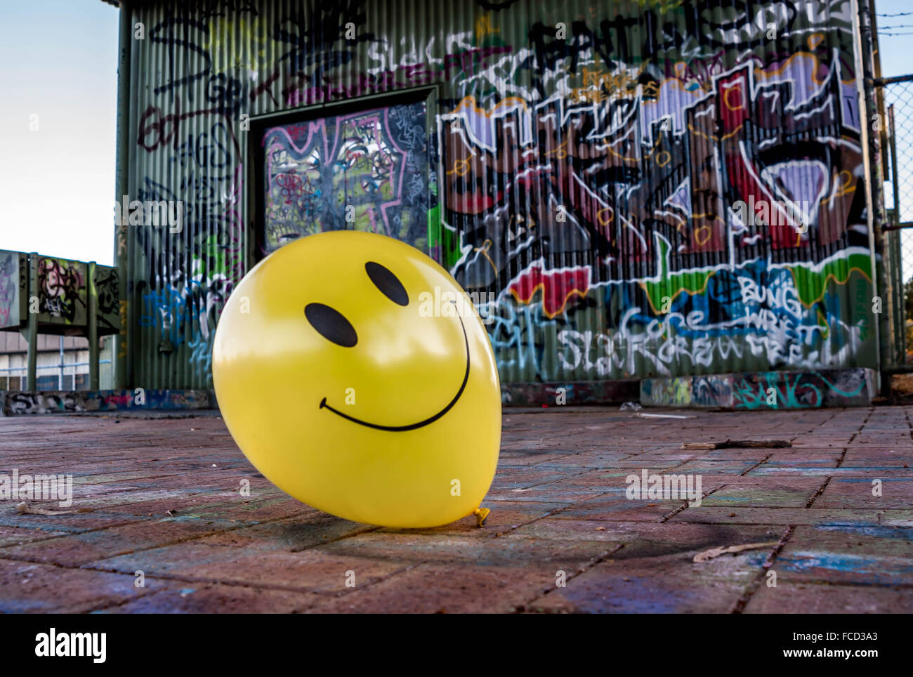 Ballon jaune avec smiley face en face du bâtiment avec de la peinture aérosol graffiti Banque D'Images