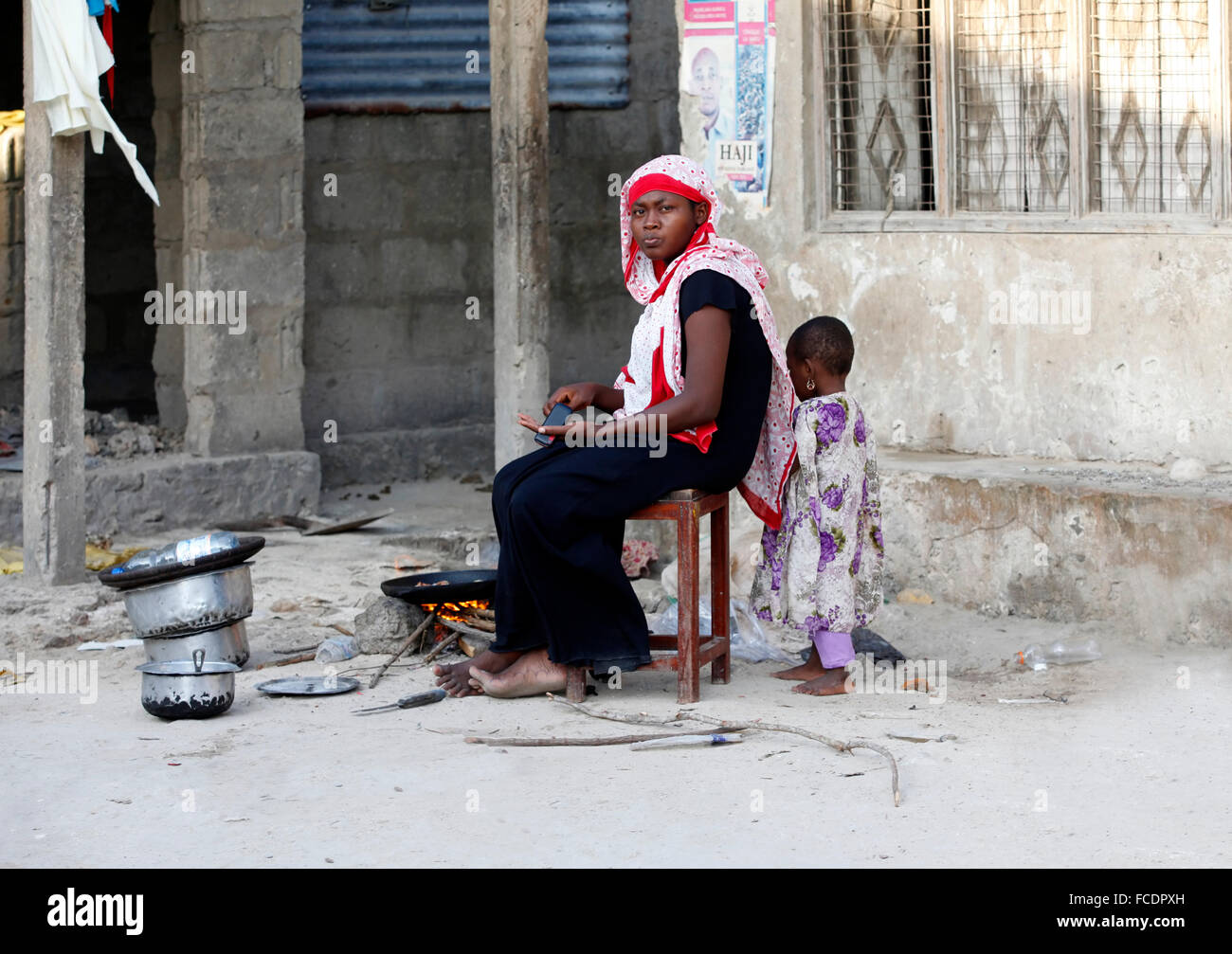 Zanzibar, Tanzanie - 9 janvier 2016 : femme musulmane à cuisiniers près de sa maison, son enfant joue à proximité. Siège traditionnel Banque D'Images
