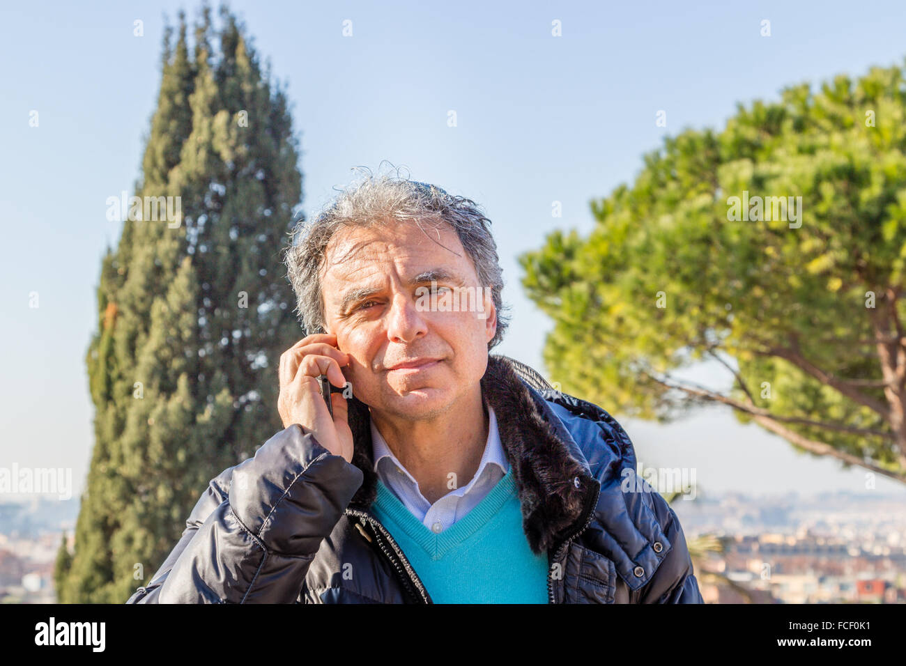 Homme de race blanche d'âge moyen aux cheveux gris vêtus de noir Down jacket talking on phone Banque D'Images