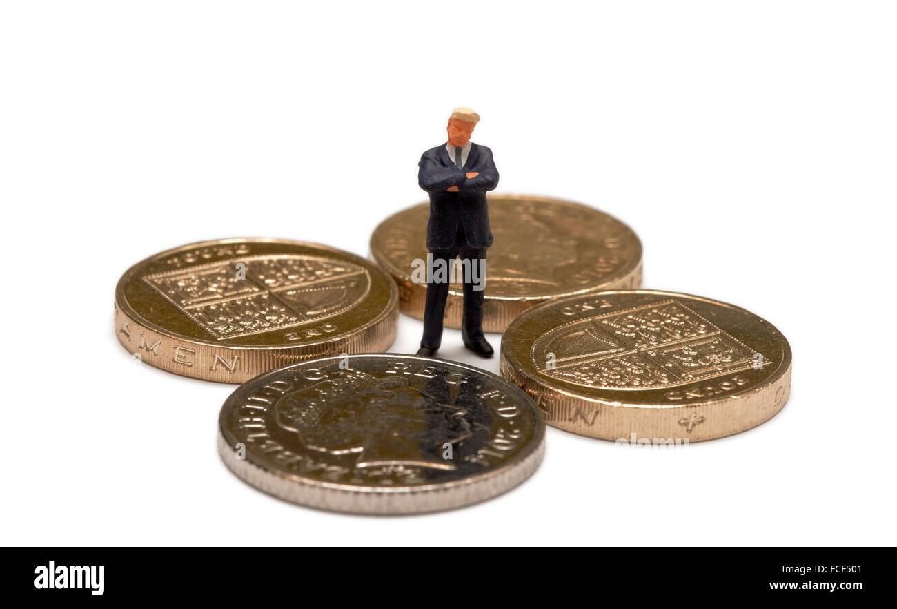 Figurine miniature d'un homme en costume se tenant debout à l'intérieur pièces livre et une pièce de 10 pence with arms folded Banque D'Images