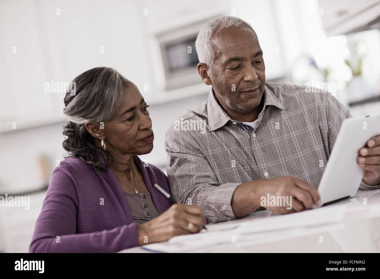 Un couple assis à une table à côté de l'autre, à l'aide d'une tablette numérique, regarder l'écran. Banque D'Images