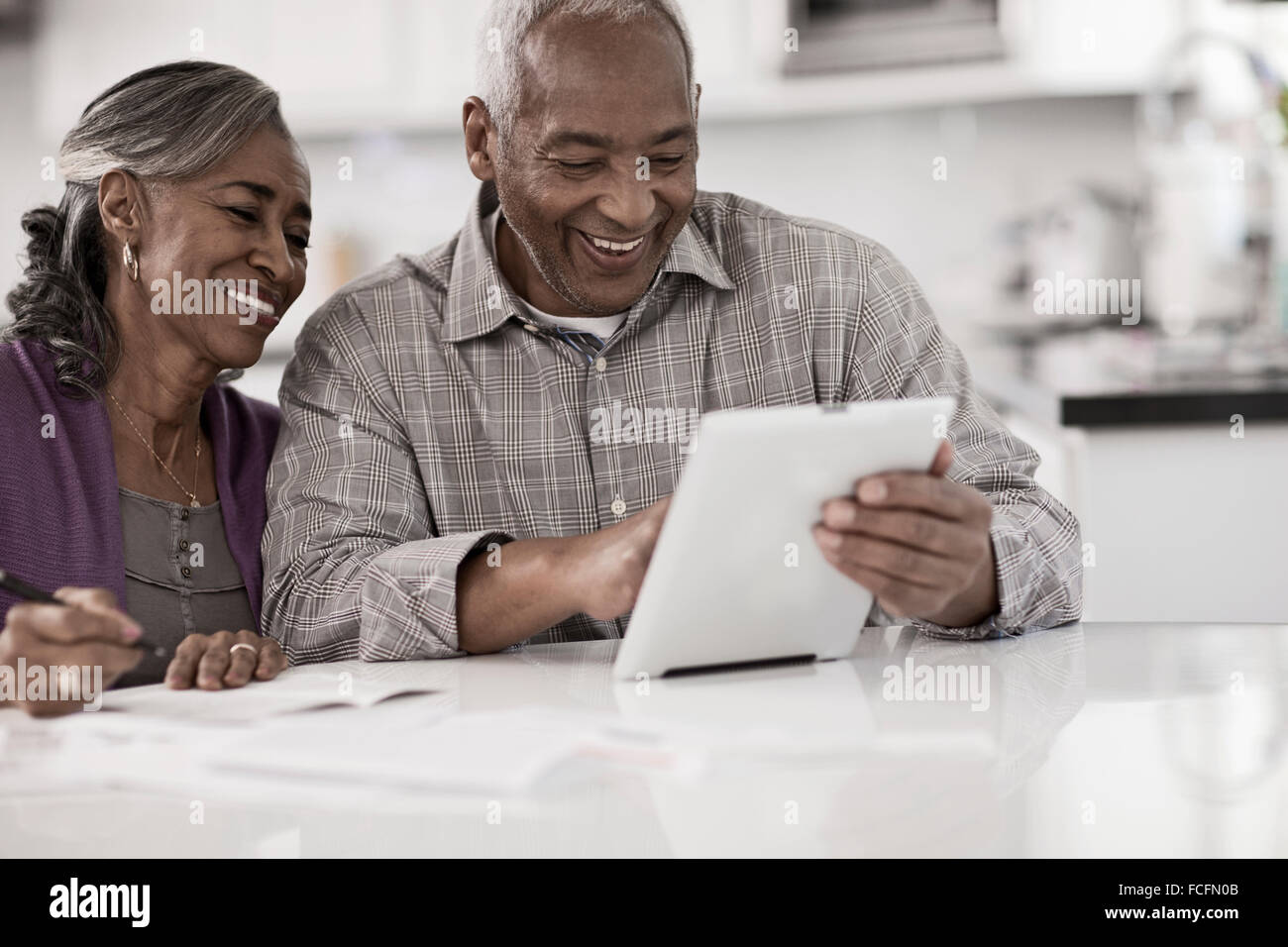 Un couple assis à une table à côté de l'autre, à l'aide d'une tablette numérique, regarder l'écran. Banque D'Images