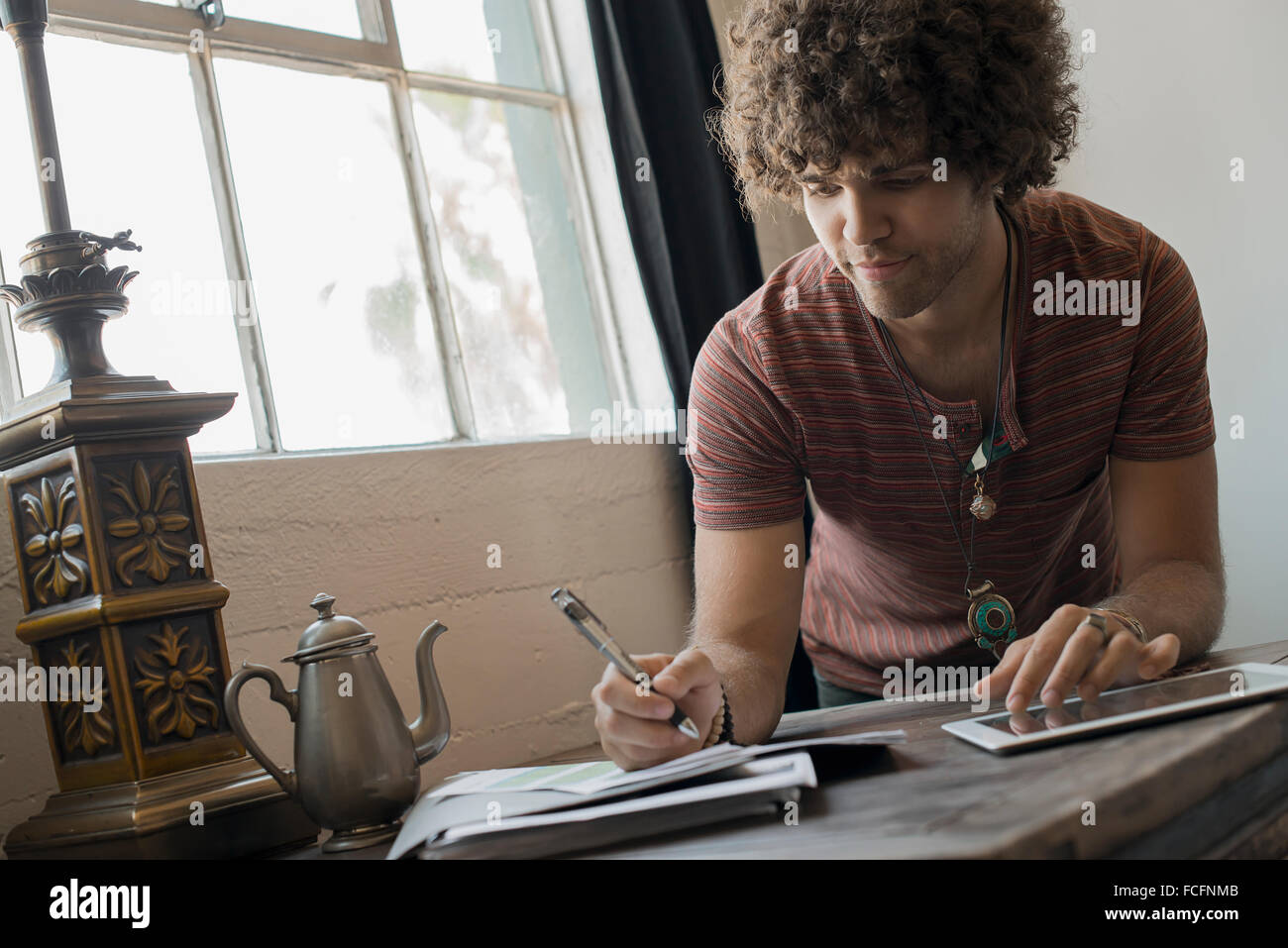 Loft vivant. Un homme assis par fenêtre, utiliser du papier et un crayon et une tablette numérique. Banque D'Images