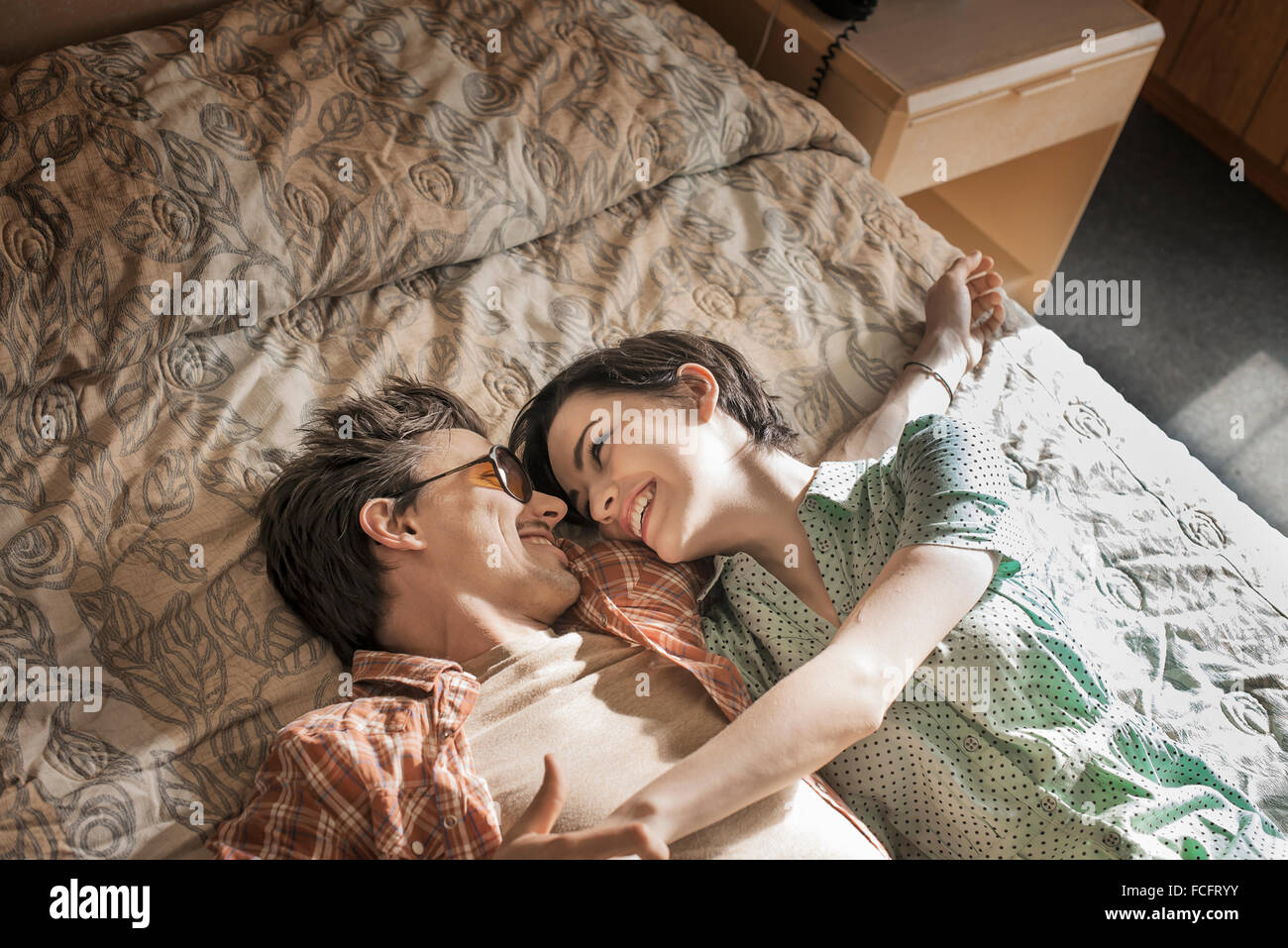 Un jeune couple couché côte à côte sur le dessus du lit dans une chambre de motel. Banque D'Images