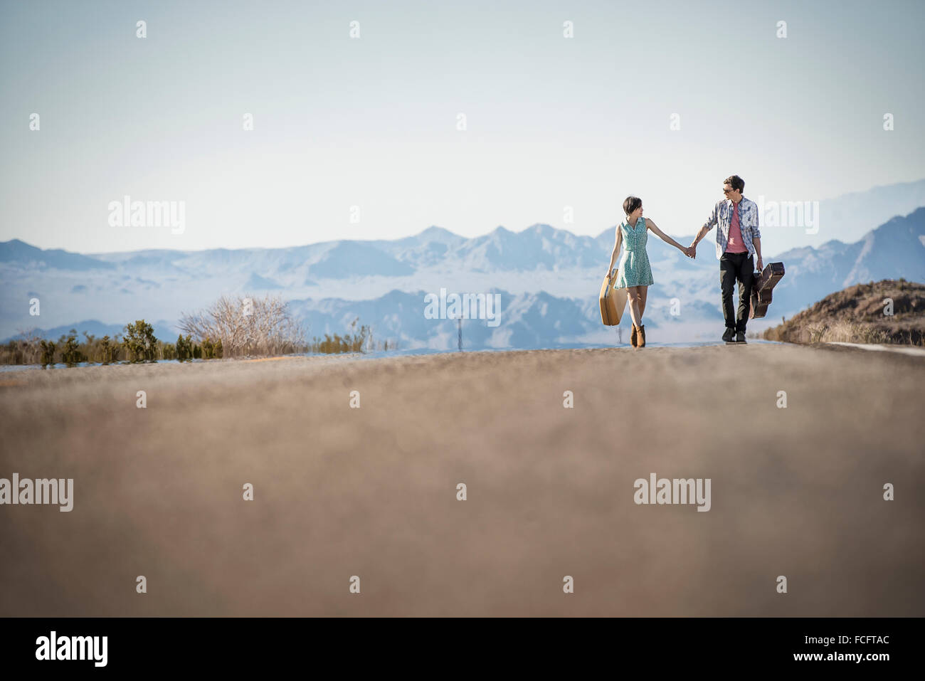 Un jeune couple, homme et femme, marche main dans la main sur une route goudronnée dans le désert des étuis de transport. Banque D'Images