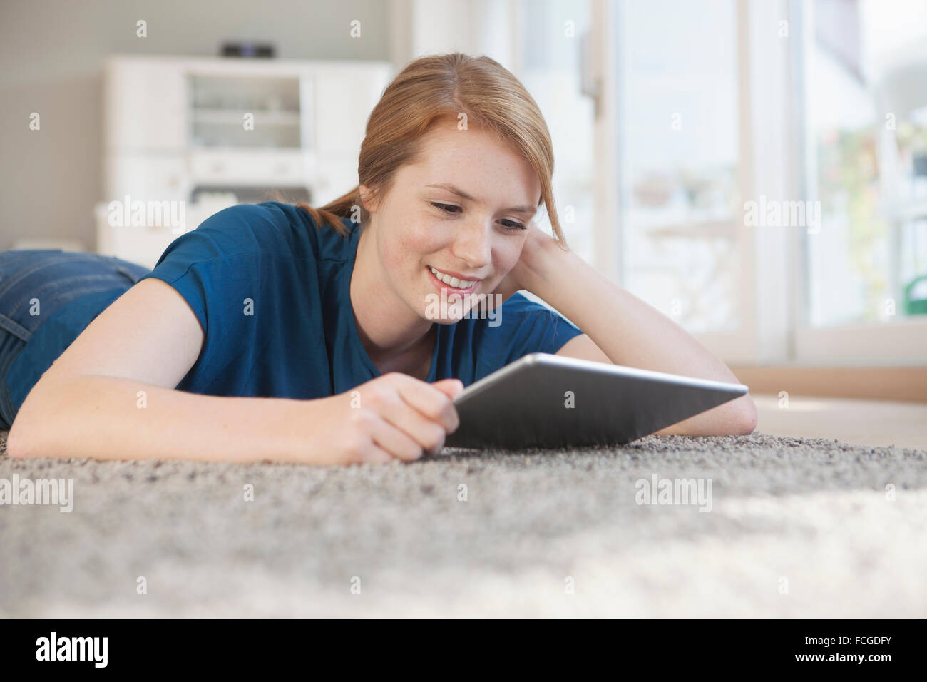 Portrait of smiling young woman relaxing tablette numérique sur le plancher à la maison Banque D'Images